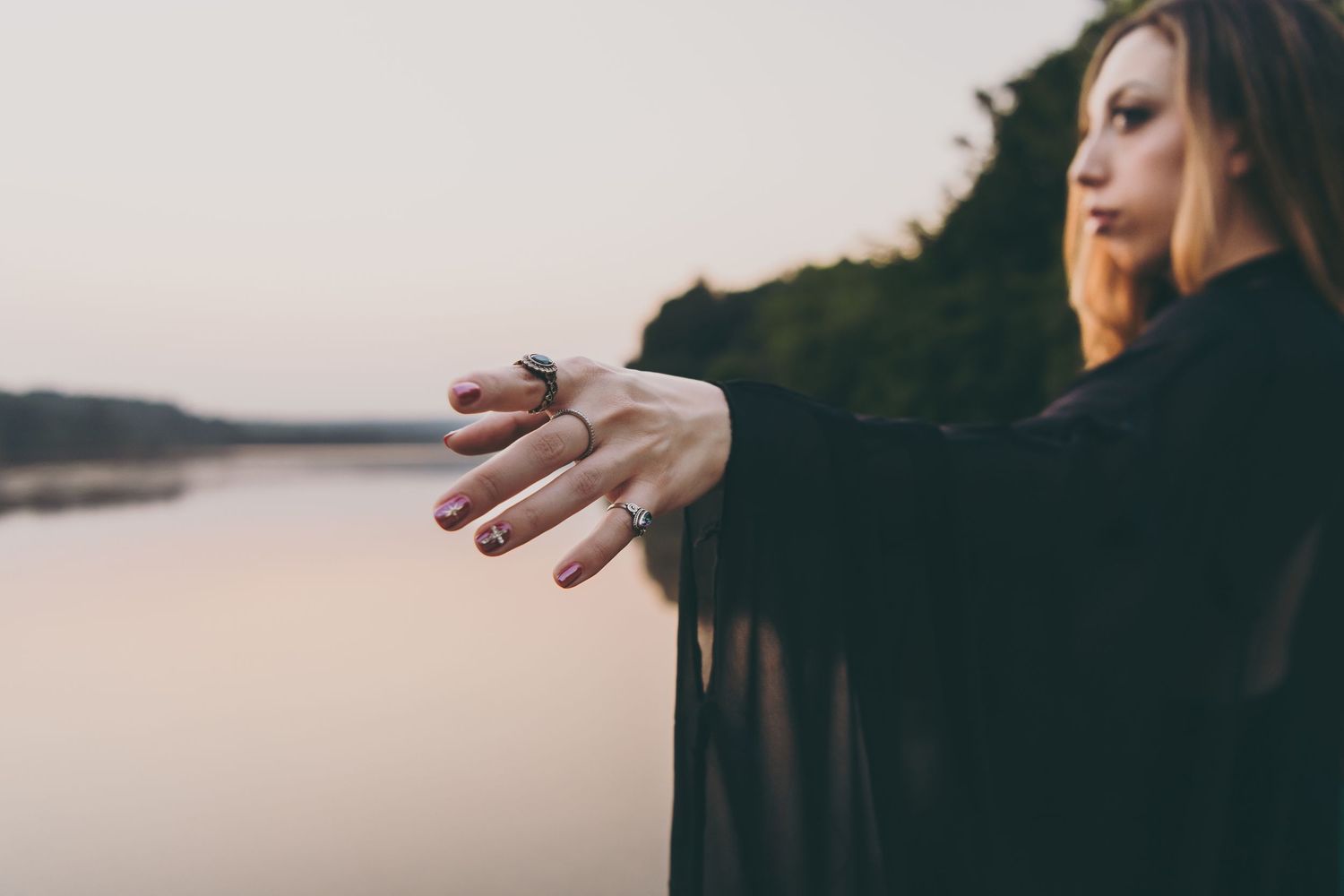 Person in black clothing extends arm against sunset lake backdrop creating artistic silhouette.