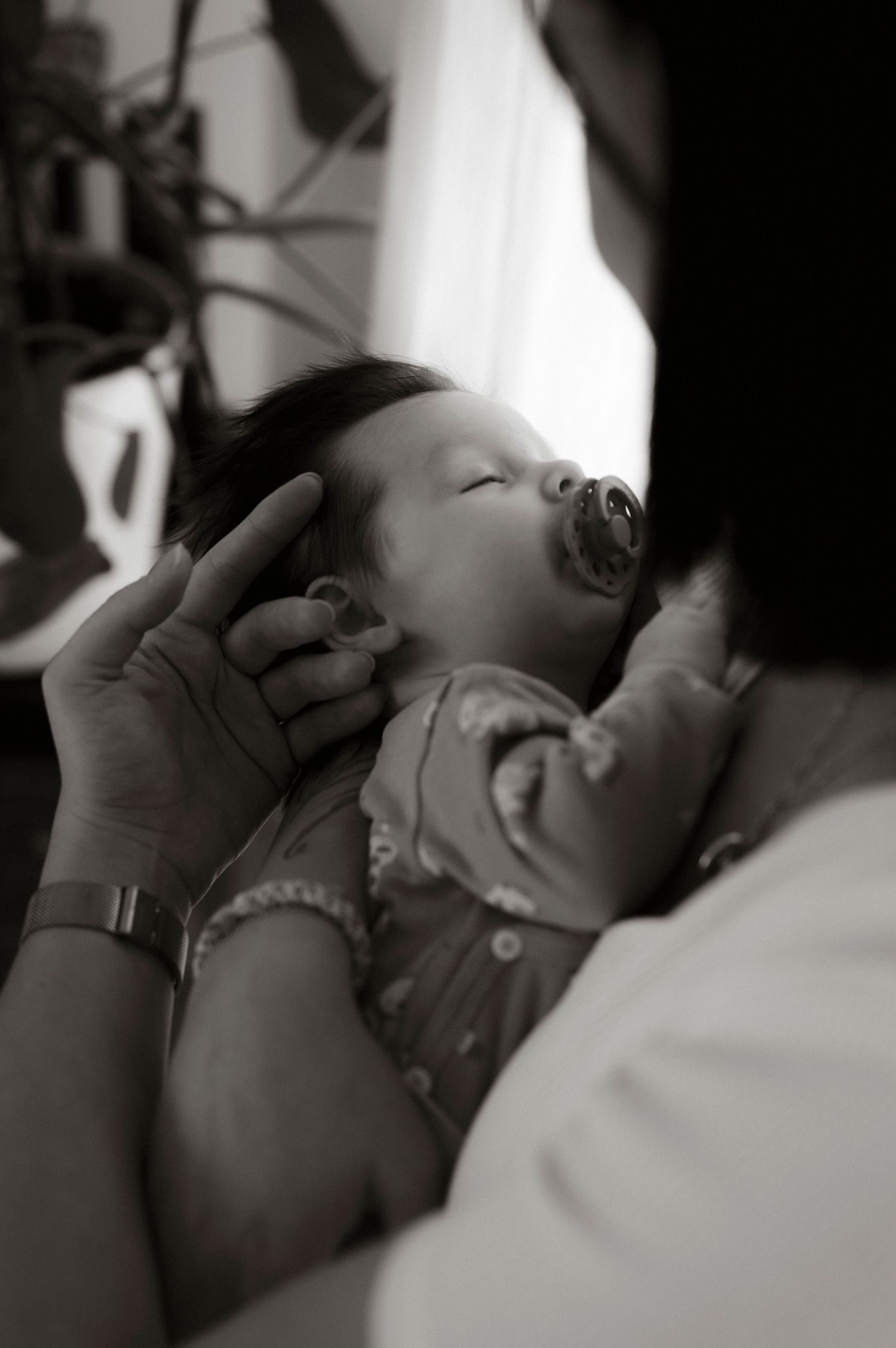 A tender black and white photo of a sleeping newborn baby being cradled by gentle hands.