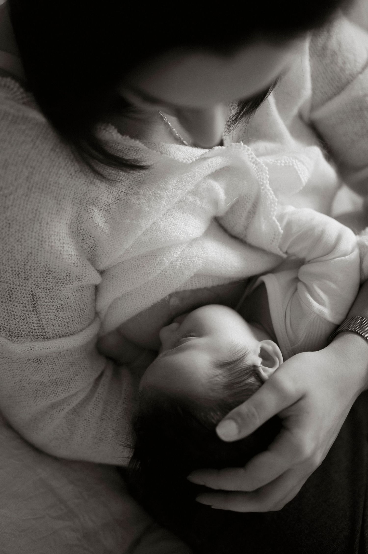 A tender black and white photography of a cradled newborn wrapped in soft white fabric.