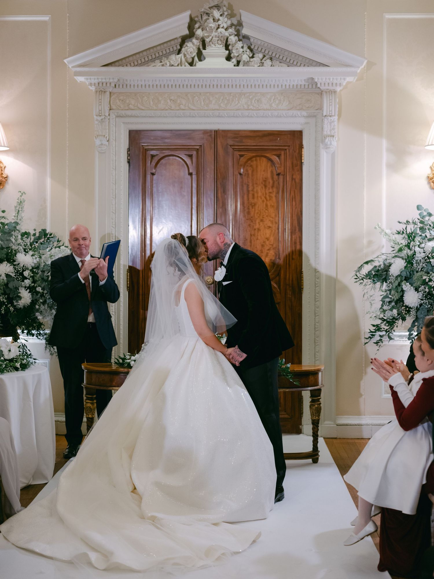Traditional church wedding ceremony with an ornate white doorway and greenery decorations framing the romantic moment.