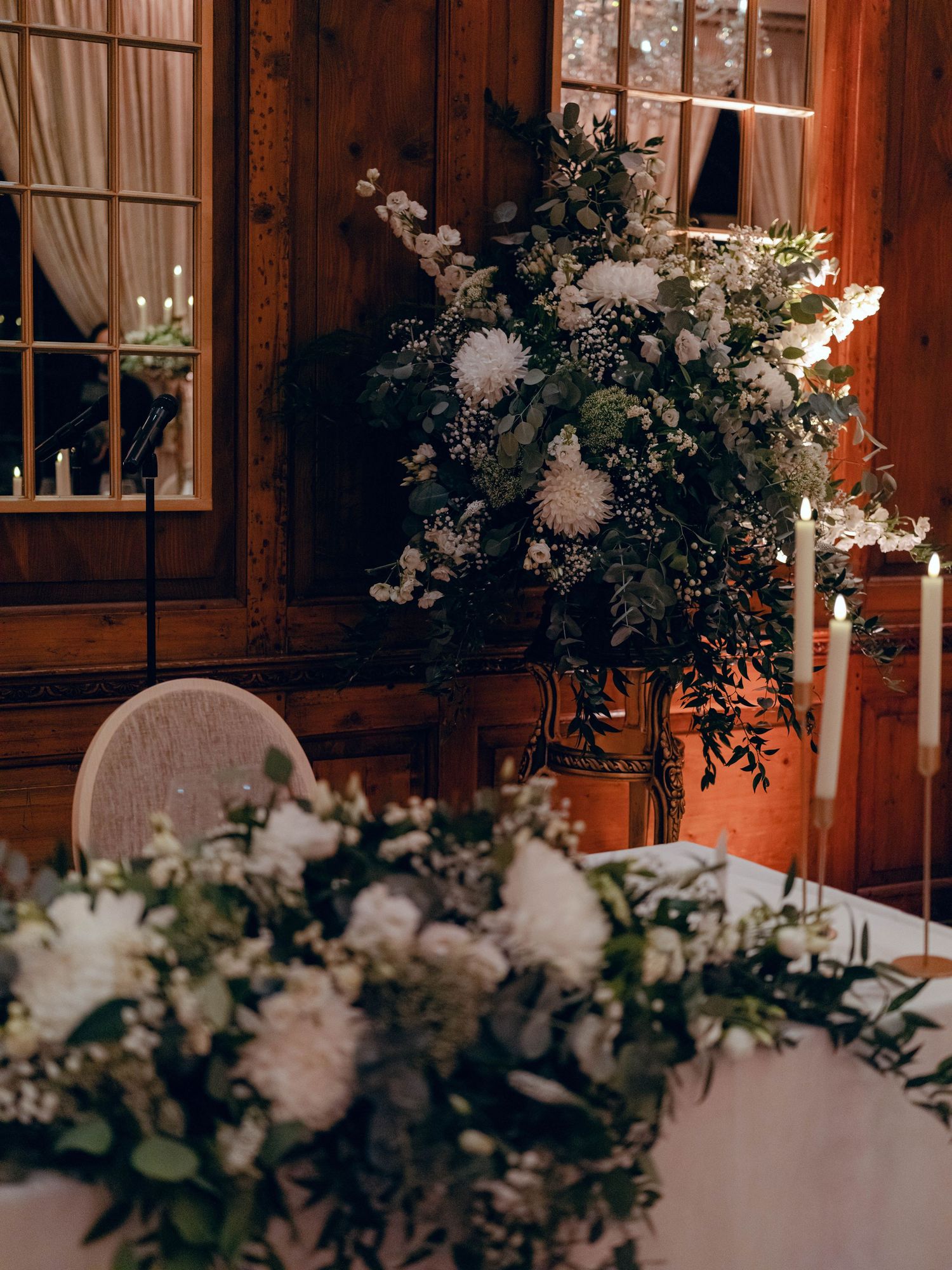 Elegant floral arrangements with white flowers and greenery adorn a wooden interior with candlelight and luminous ambiance.