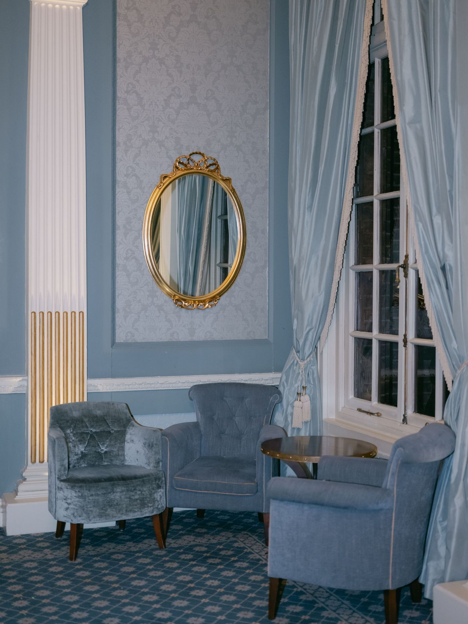 Elegant sitting area with blue velvet armchairs, white columns, and ornate gold mirror in a classic Georgian-style room.