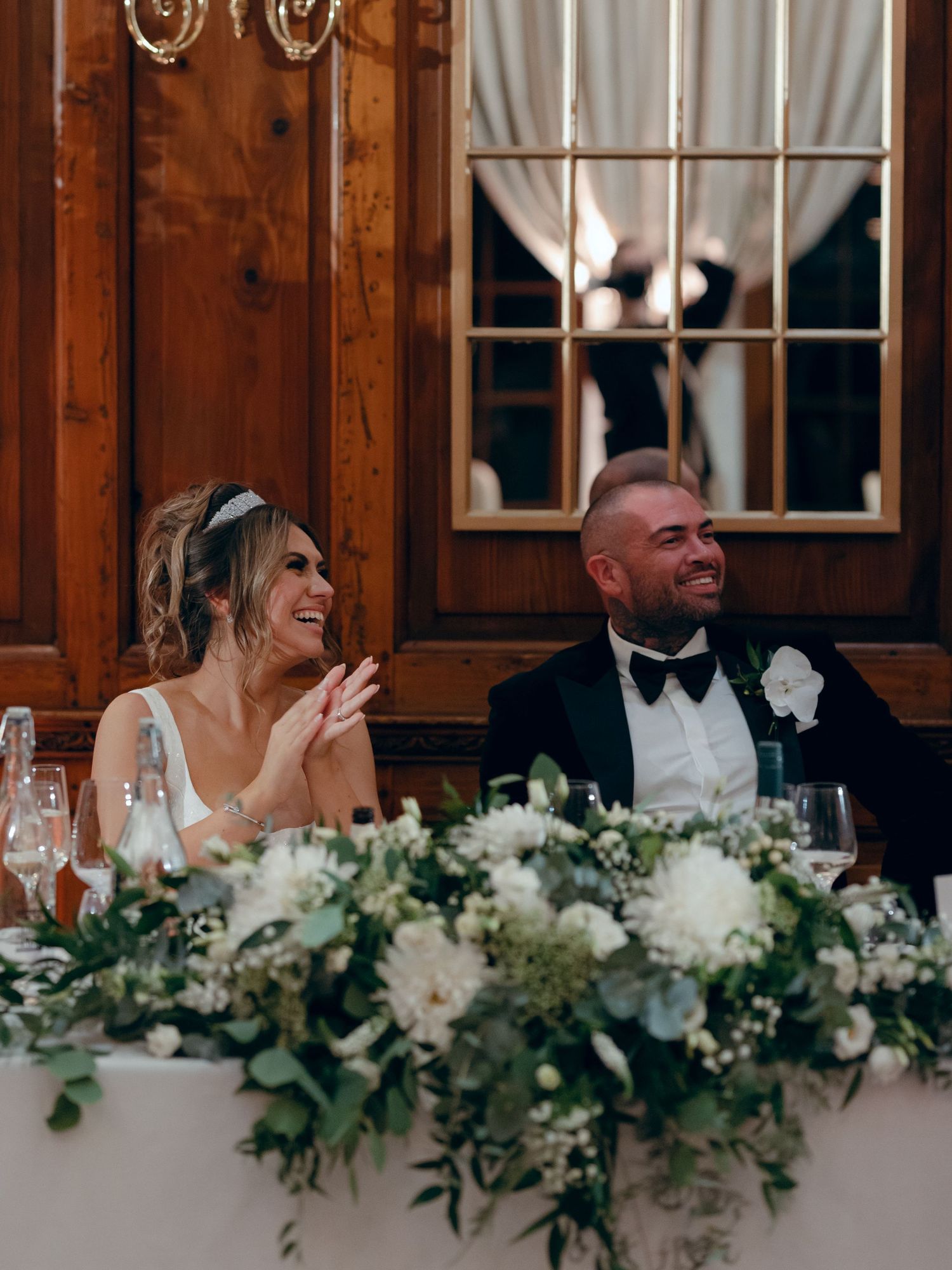 A happily married couple shares a candid moment at their wedding reception with elegant white floral table decorations.