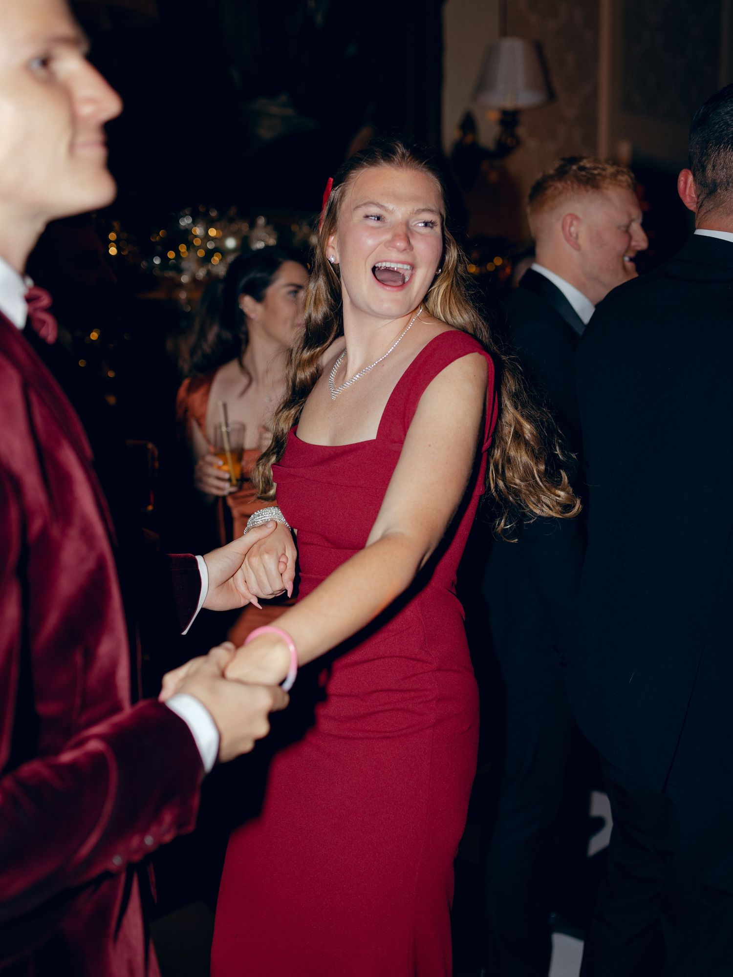 A person in a red dress laughs joyfully while dancing at an elegant evening party.