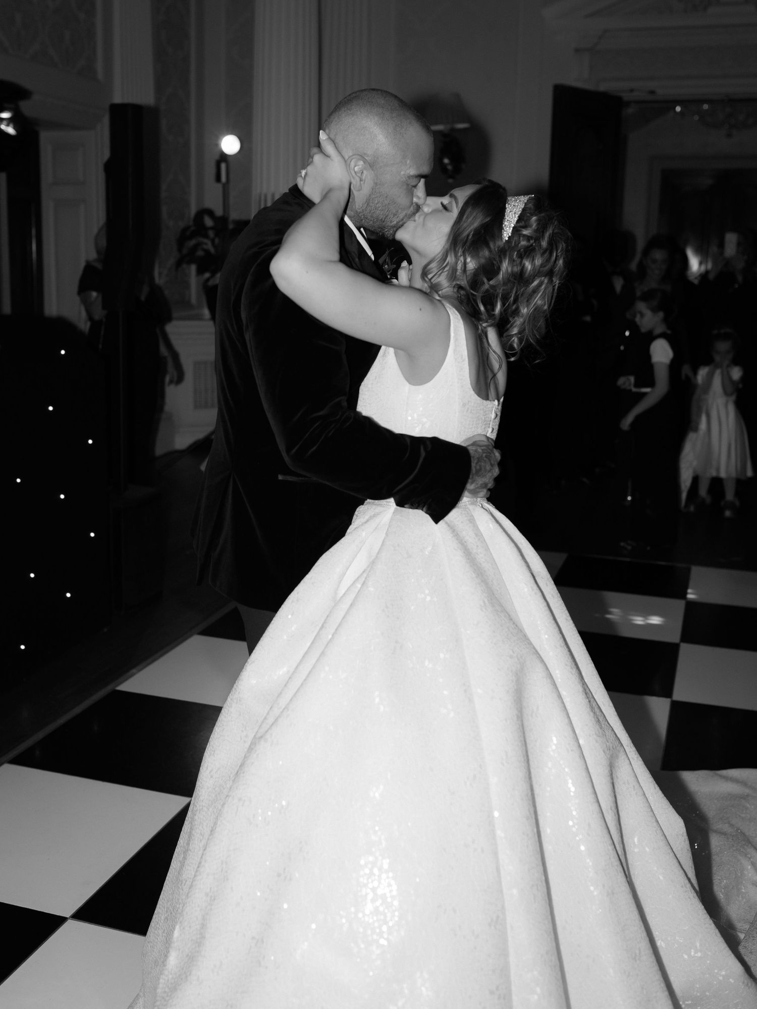 A couple in monochrome shares their first dance at a wedding reception on a black and white checkered dance floor.