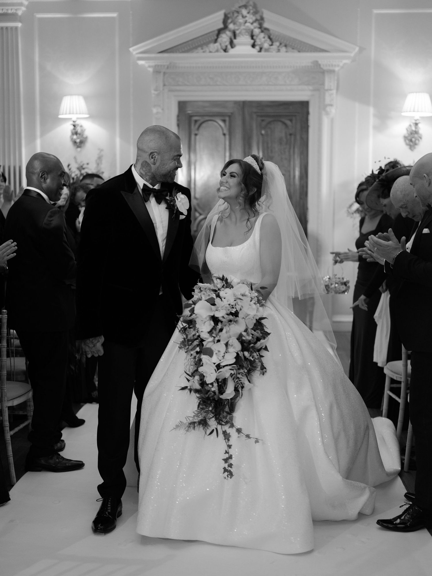 A couple shares an intimate moment at their elegant black and white wedding ceremony in a grand room with classic decor.