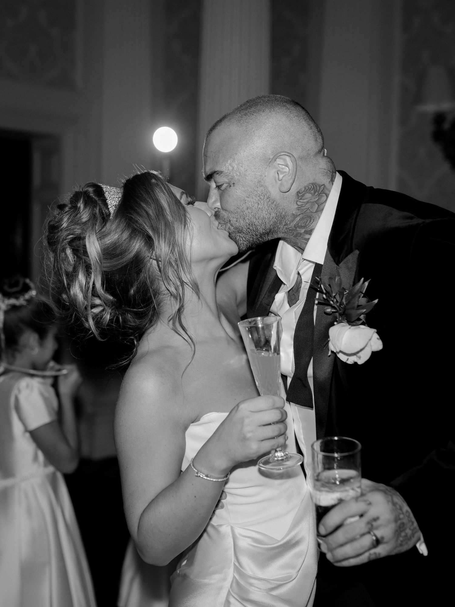 A romantic black and white wedding photo showing a couple sharing a kiss while holding champagne flutes at their reception.