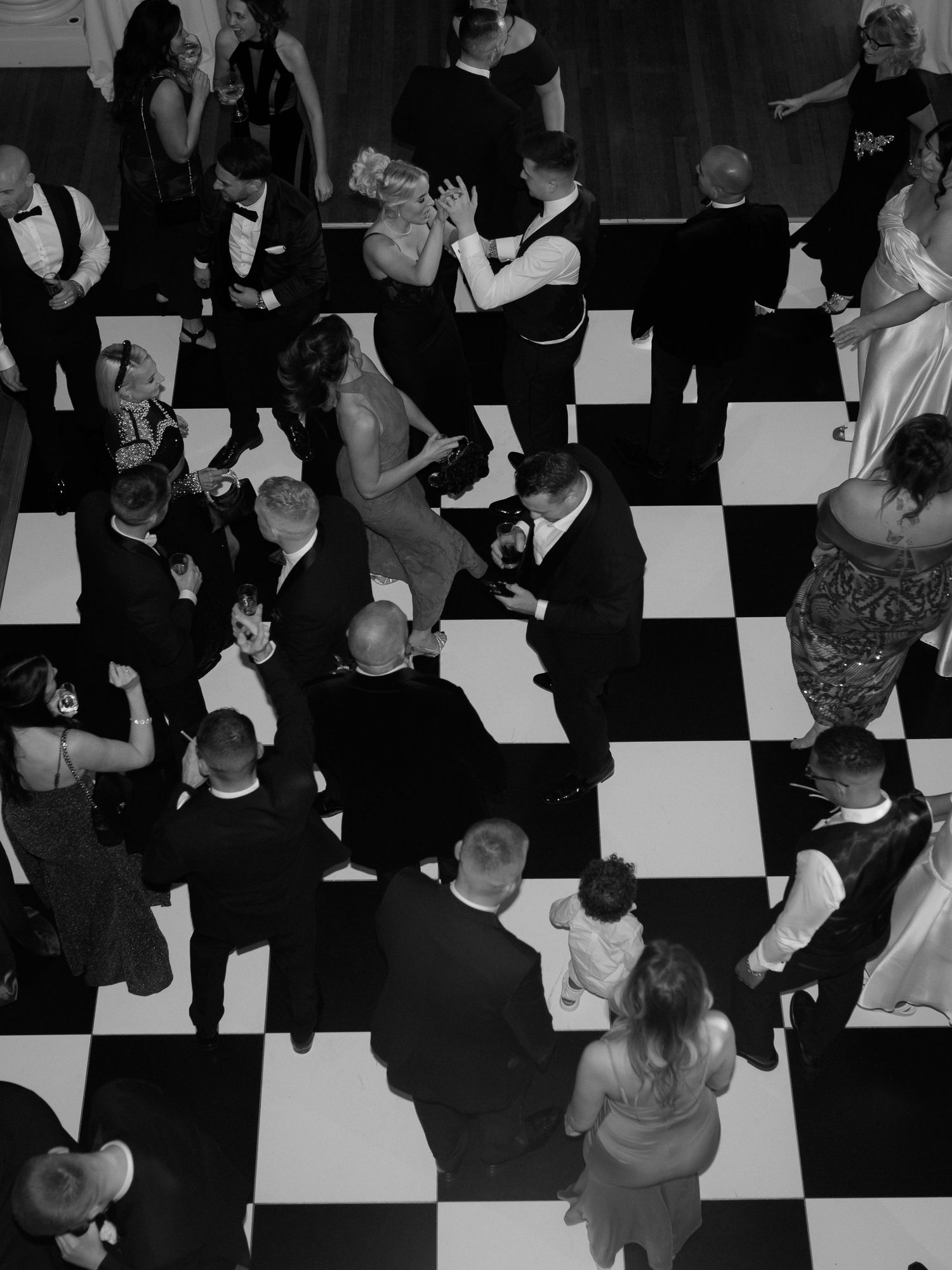 Couples dancing on a black and white checkered dance floor at a formal event, seen from above.