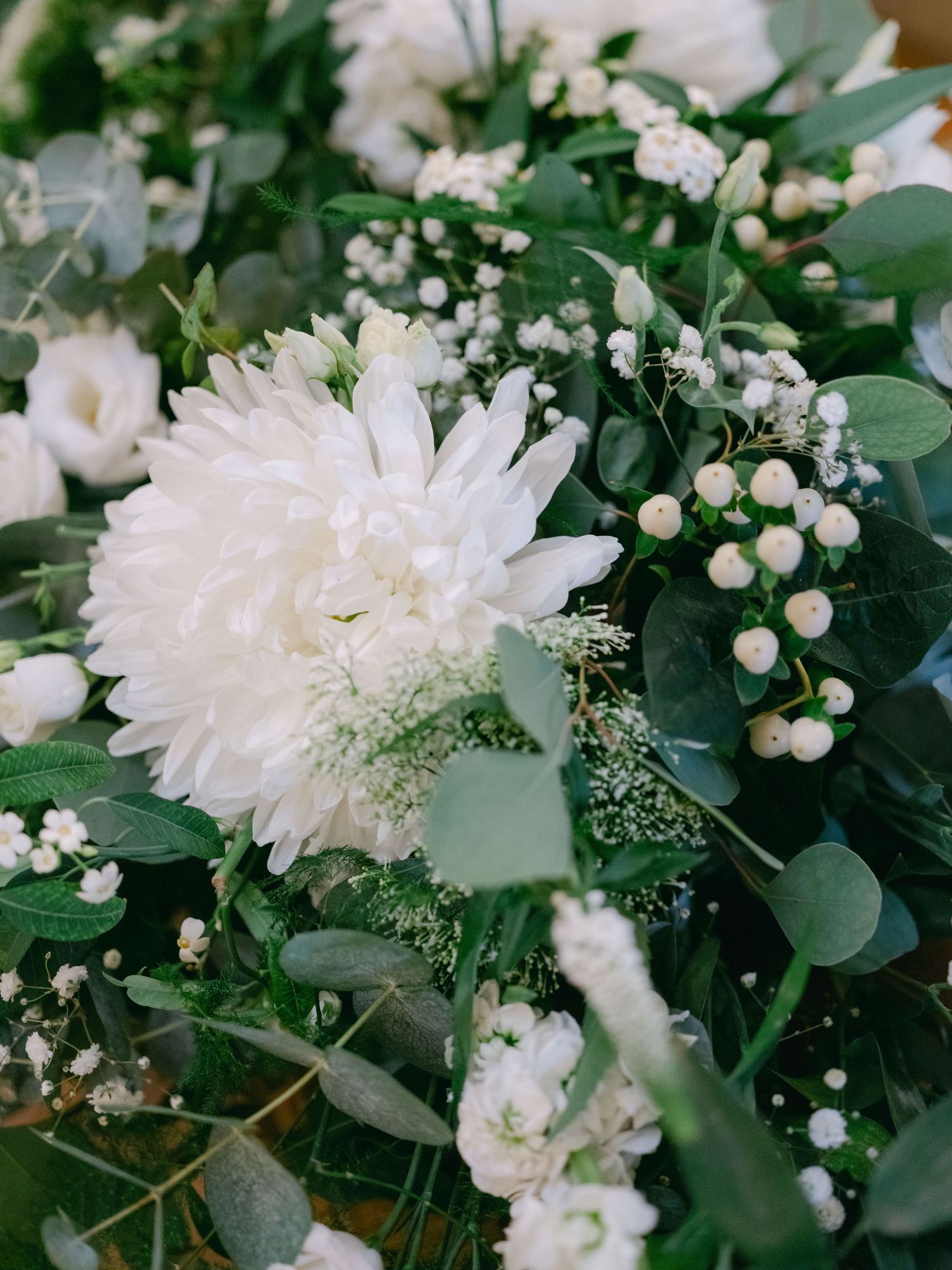 White chrysanthemum and baby's breath flower arrangement with lush green eucalyptus leaves in an elegant bouquet.