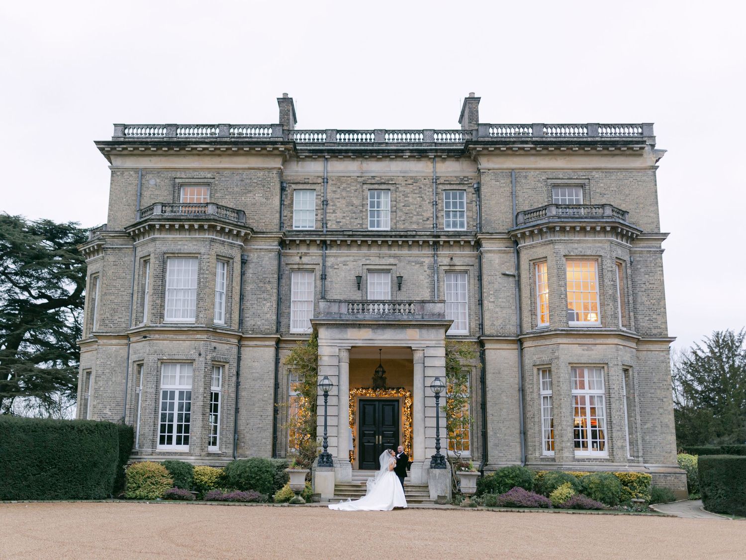 A grand Victorian-style mansion with stone facade and elegant entrance stairway illuminated at dusk.