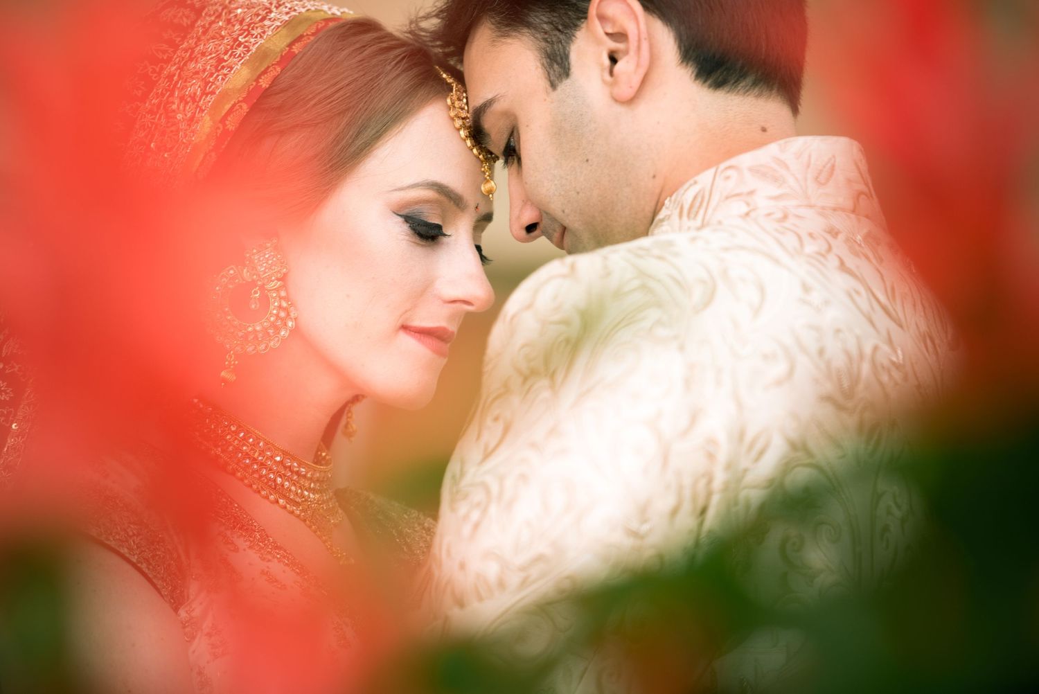 A romantic couple share an intimate moment framed by red bokeh lighting effects in a soft focus portrait.