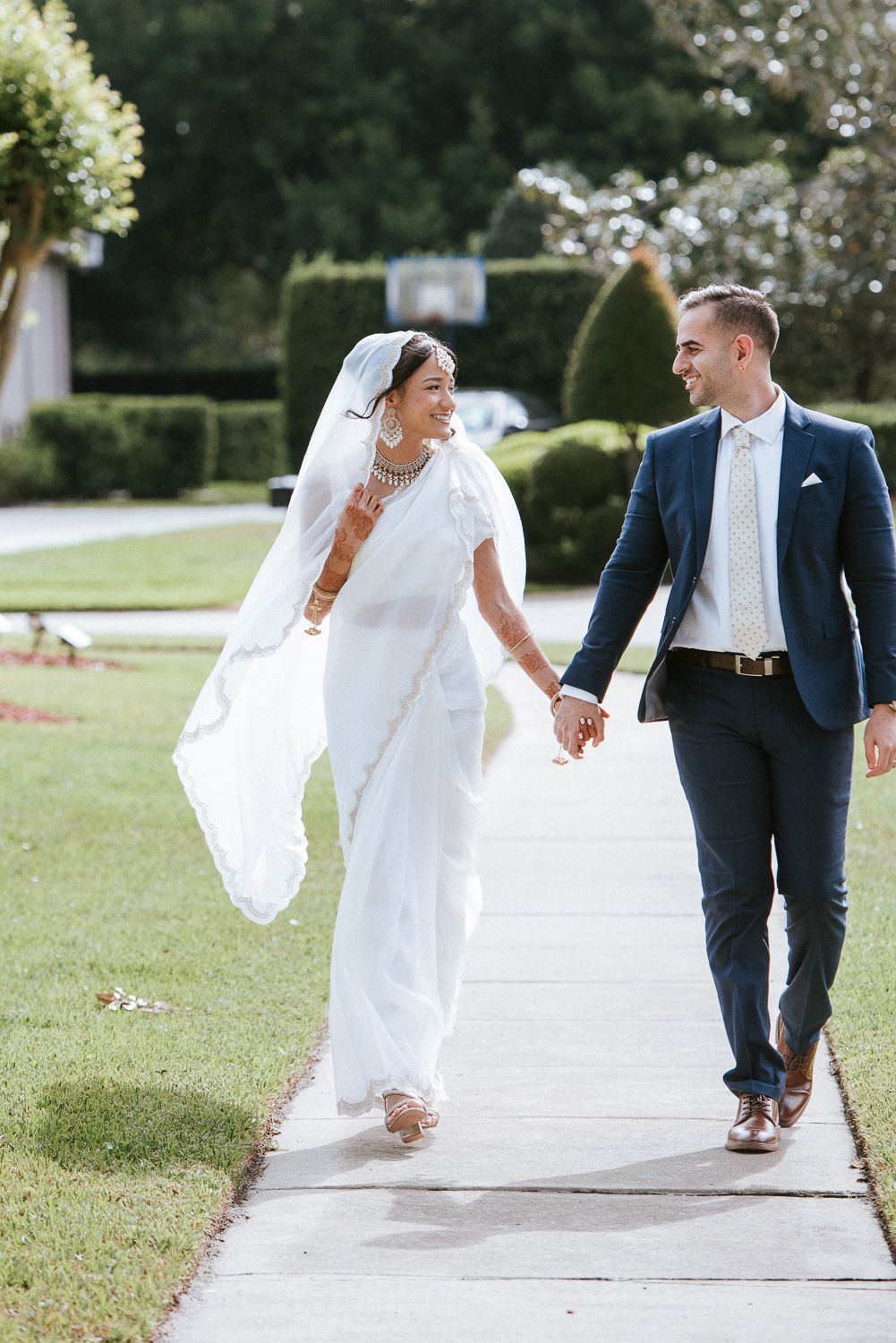 Newlyweds walking hand in hand along a garden pathway.