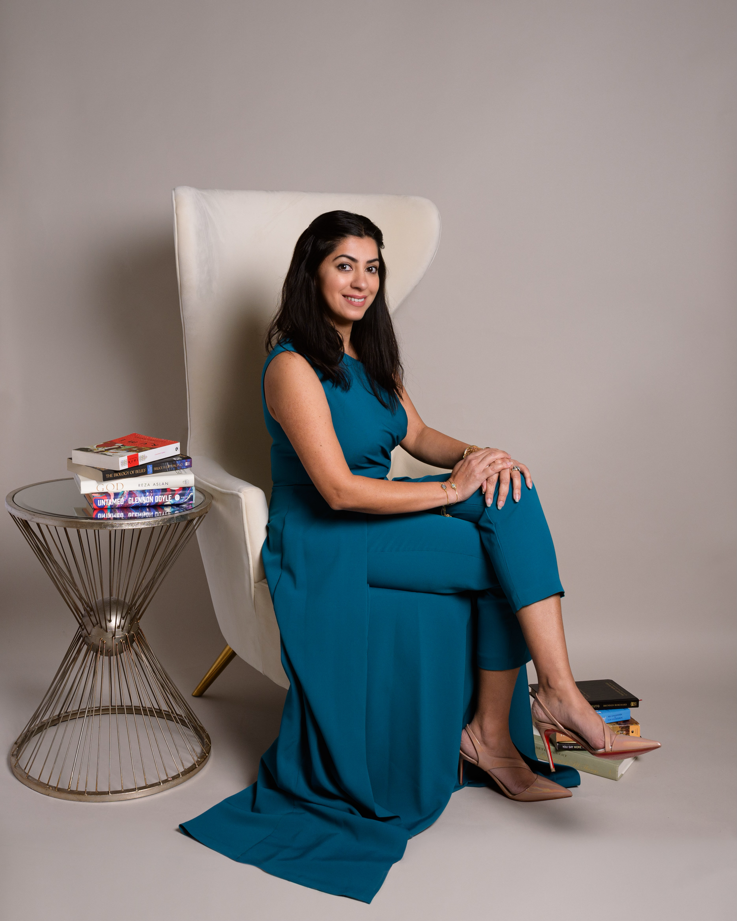 Studio portrait of woman in teal dress seated elegantly with books.