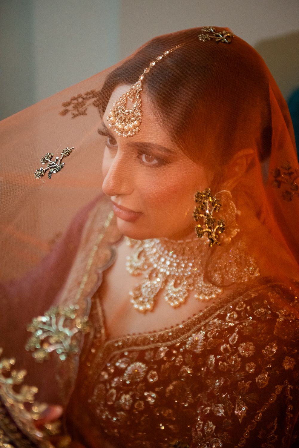Close-up portrait showcasing intricate bridal jewelry and veil details in warm golden lighting.