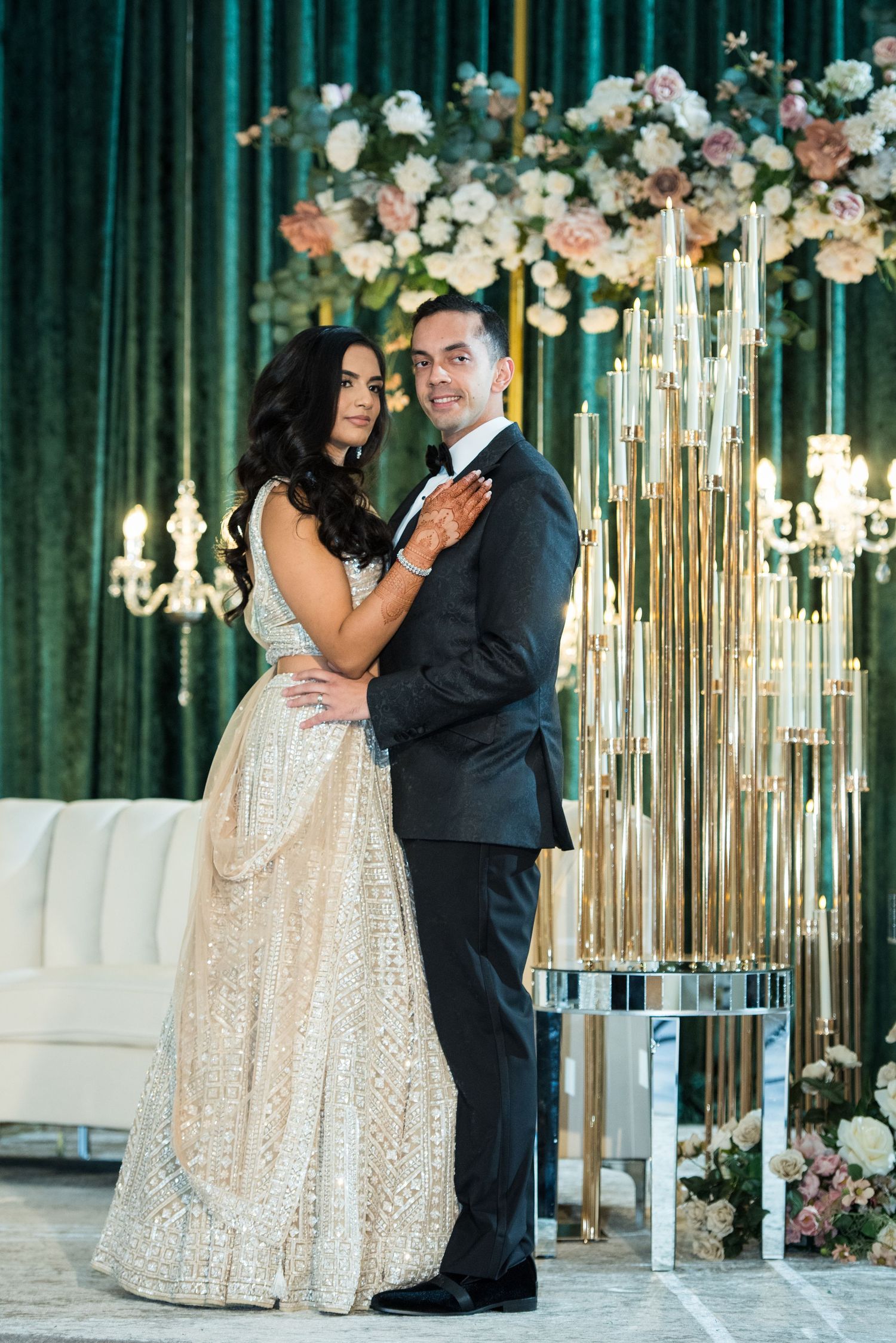 Glamorous wedding portrait with emerald backdrop, floral arrangements and gold decor elements.