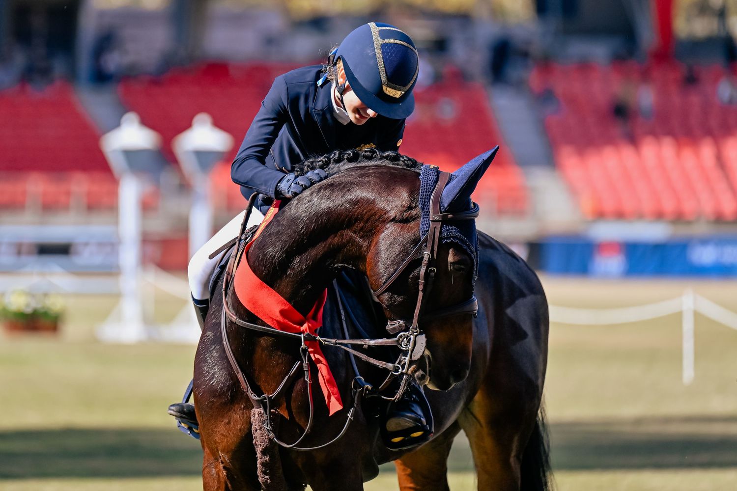 Competitive rider in navy attire in saddle patting horse during equestrian event.