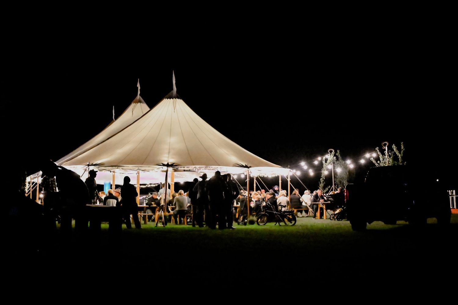 Event tents are illuminated at night, capturing a lively atmosphere against the dark sky.