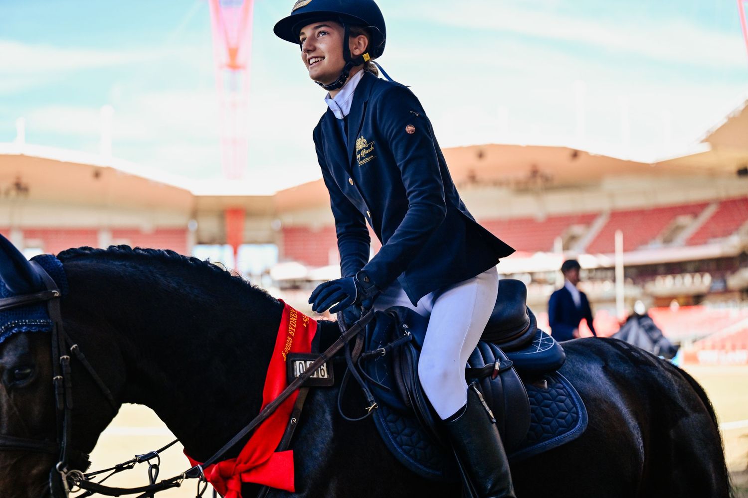 Riders in formal equestrian attire competing at an outdoor jumping arena.