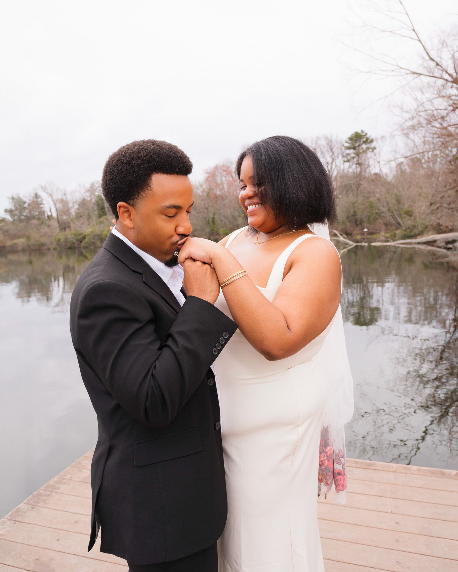 A couple shares an intimate moment together on a wooden dock by a serene lake during their outdoor wedding photo session.