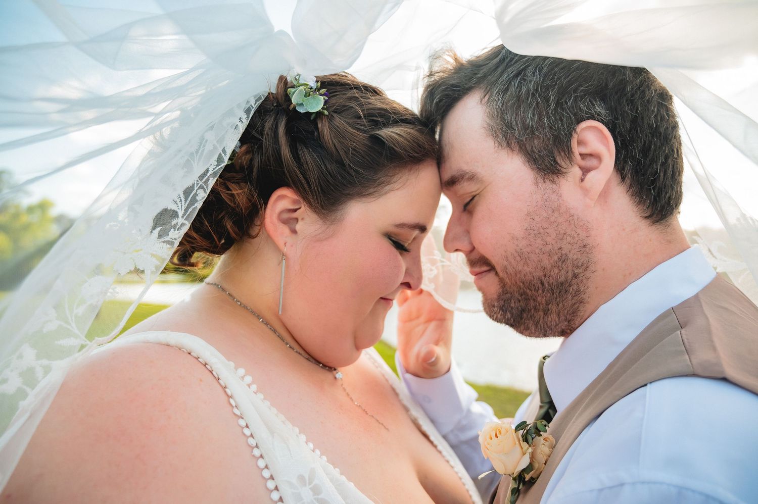A tender wedding moment captured outdoors with a white veil flowing in the breeze.