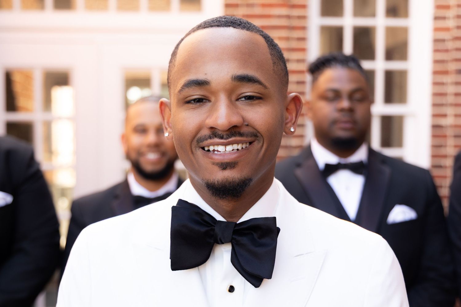 A joyful person wearing a black bow tie and white tuxedo shirt smiles brightly at a formal event.