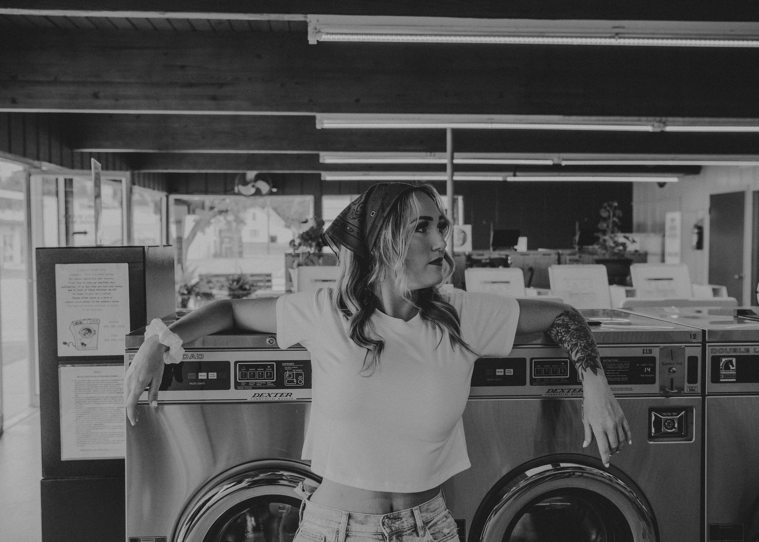 A person stands in a laundromat with washing machines in black and white vintage photograph.