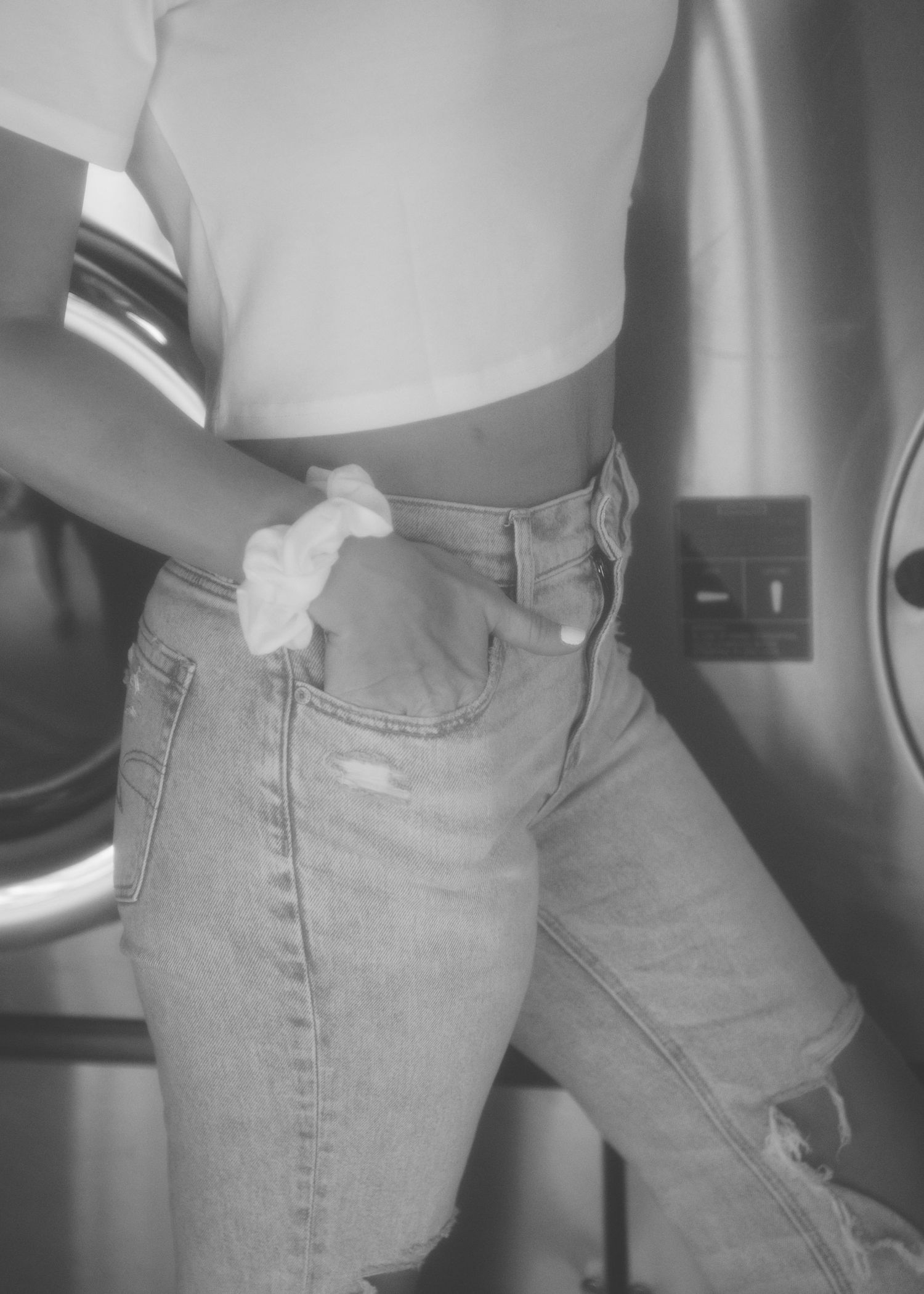 Black and white photo showing a cropped view of someone wearing high-waisted light wash distressed jeans and a white crop top.