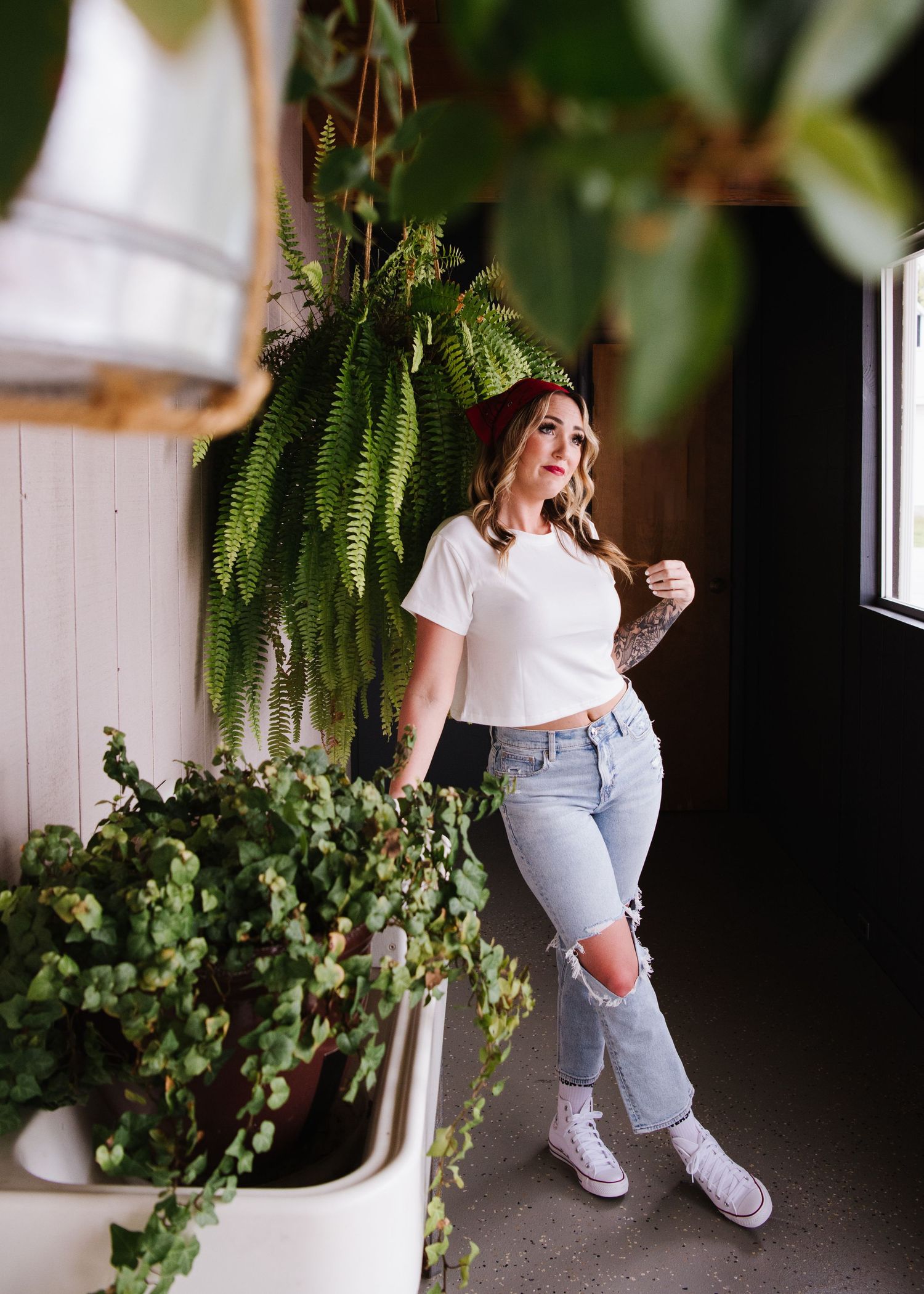 A casual lifestyle photo featuring white sneakers, distressed jeans and a houseplant in natural lighting near a window.