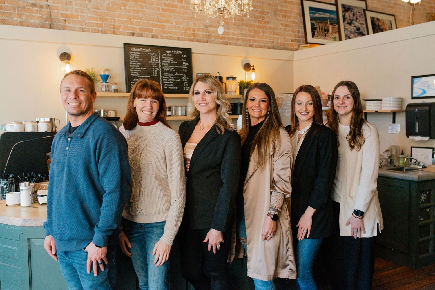 Group of professionals stand together in a cafe with exposed brick walls and warm lighting.