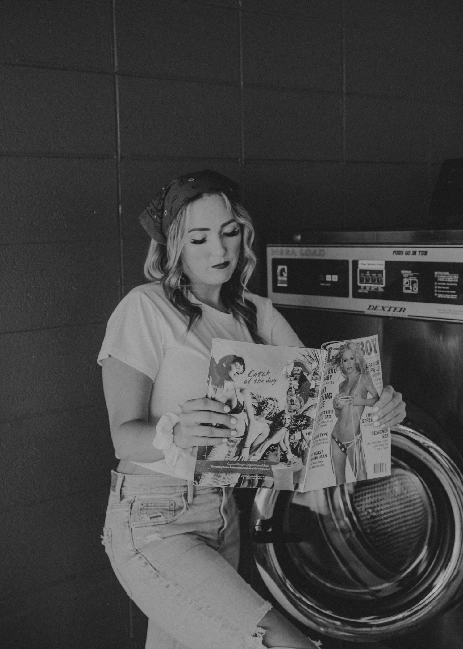 A person in a short-sleeved white shirt sits by a laundromat washing machine while reading a manga book.