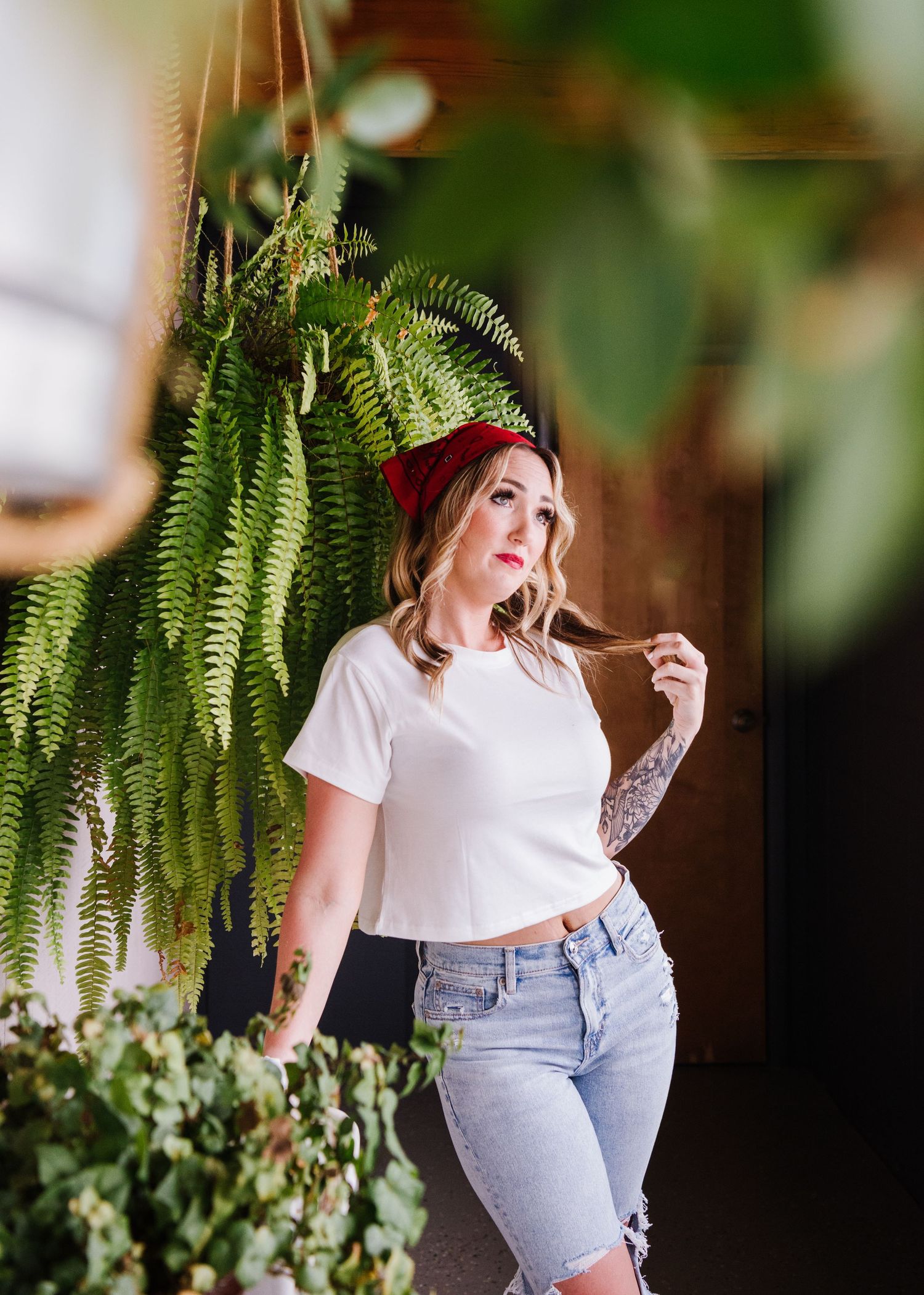 A model stands against a wall with hanging fern plants wearing a white t-shirt and light denim jeans.