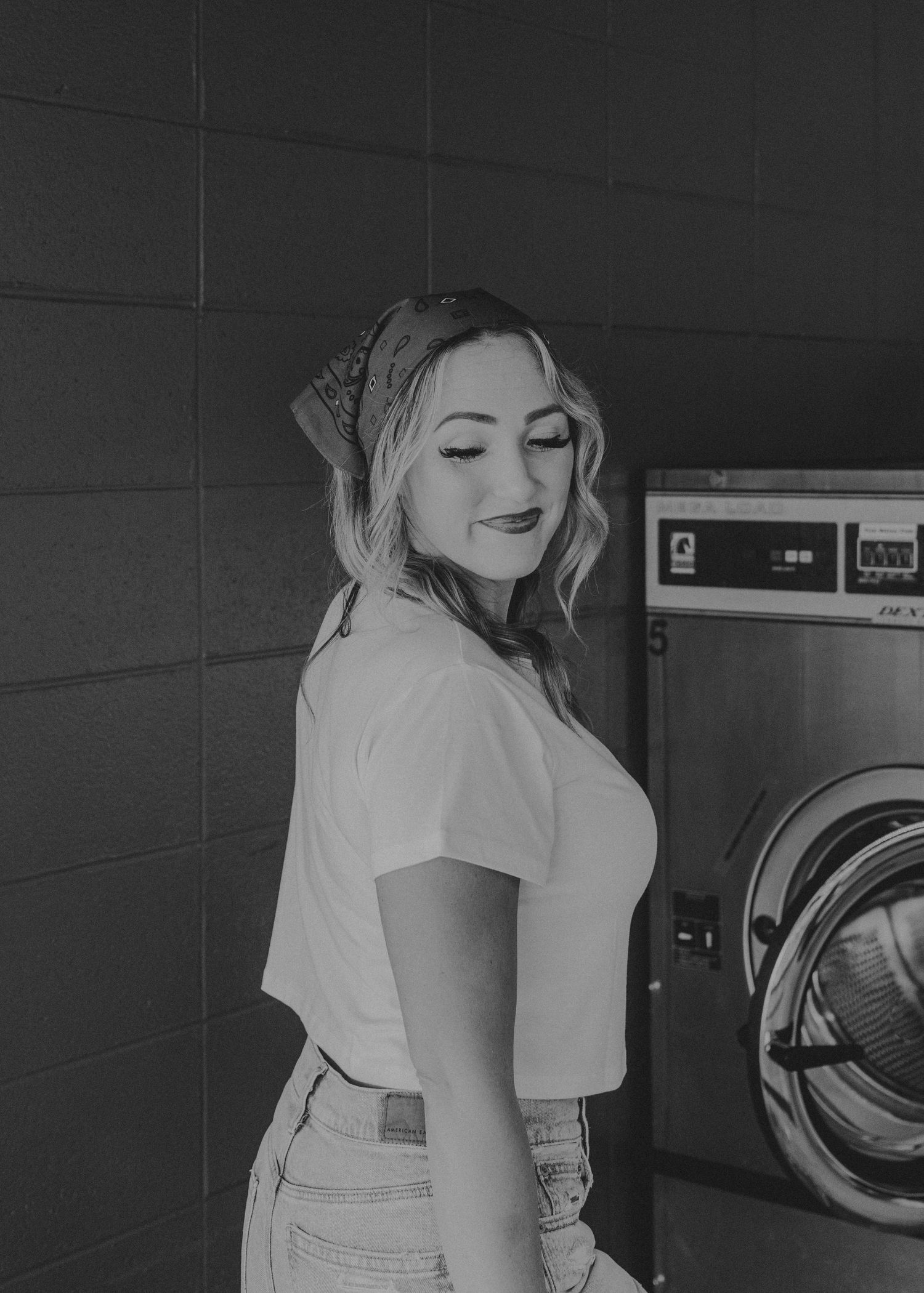 Person in white t-shirt smiling at laundromat with washing machines in black and white photography.