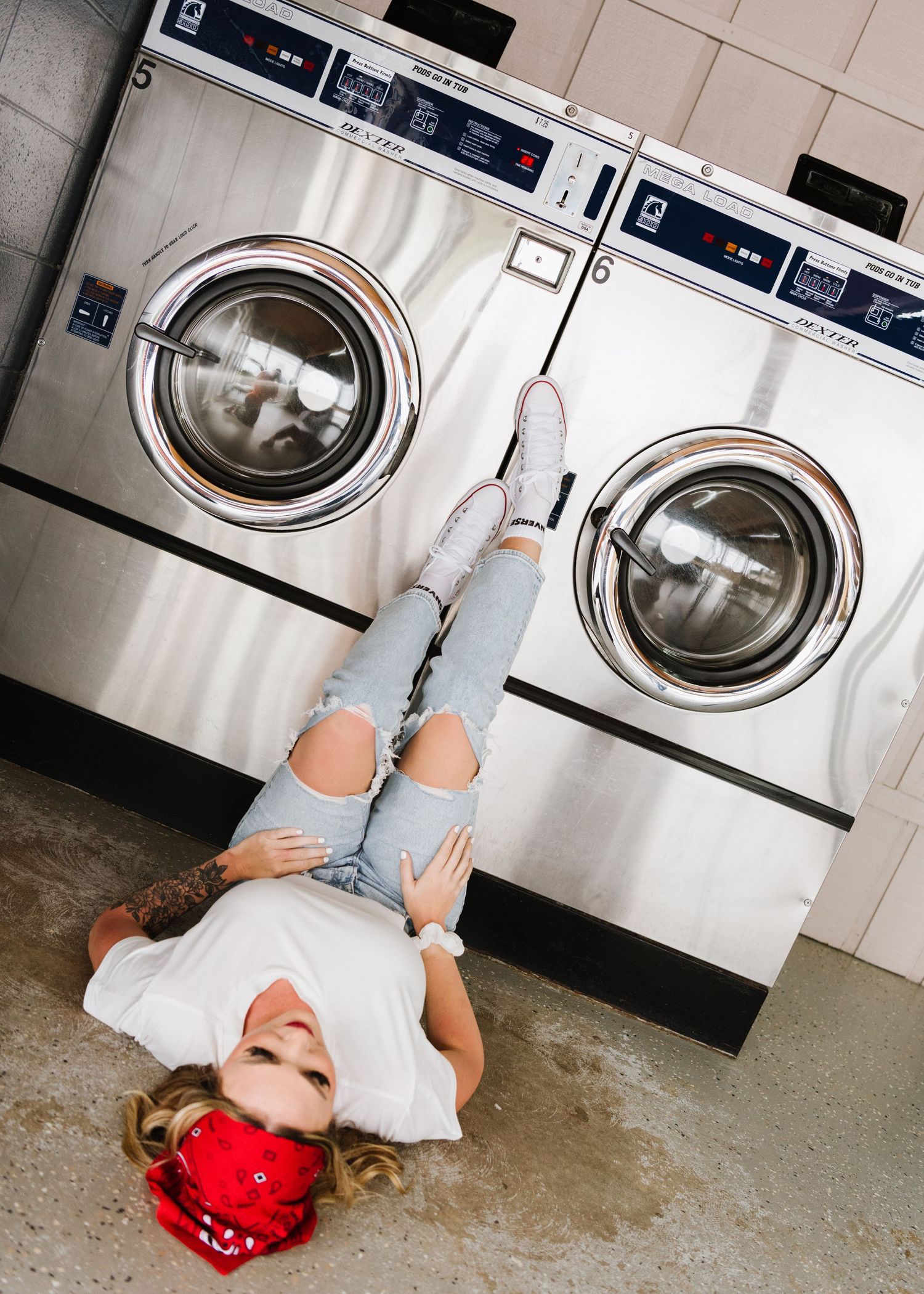 Casual laundromat scene with ripped jeans, white shirt and red bandana against industrial washing machines.