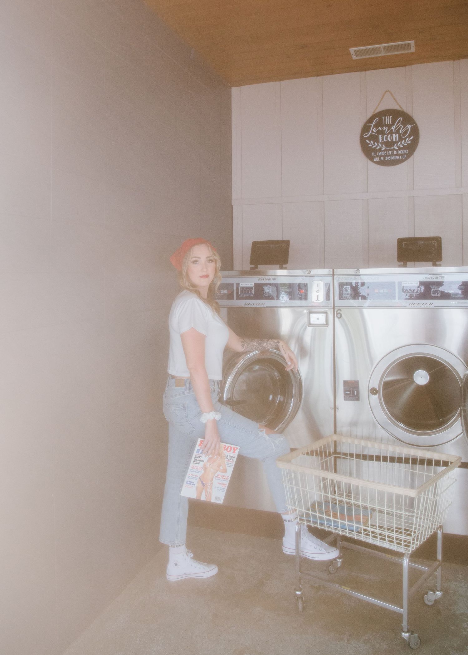 Someone in jeans and white shirt doing laundry at a retro-styled laundromat with commercial washing machines.