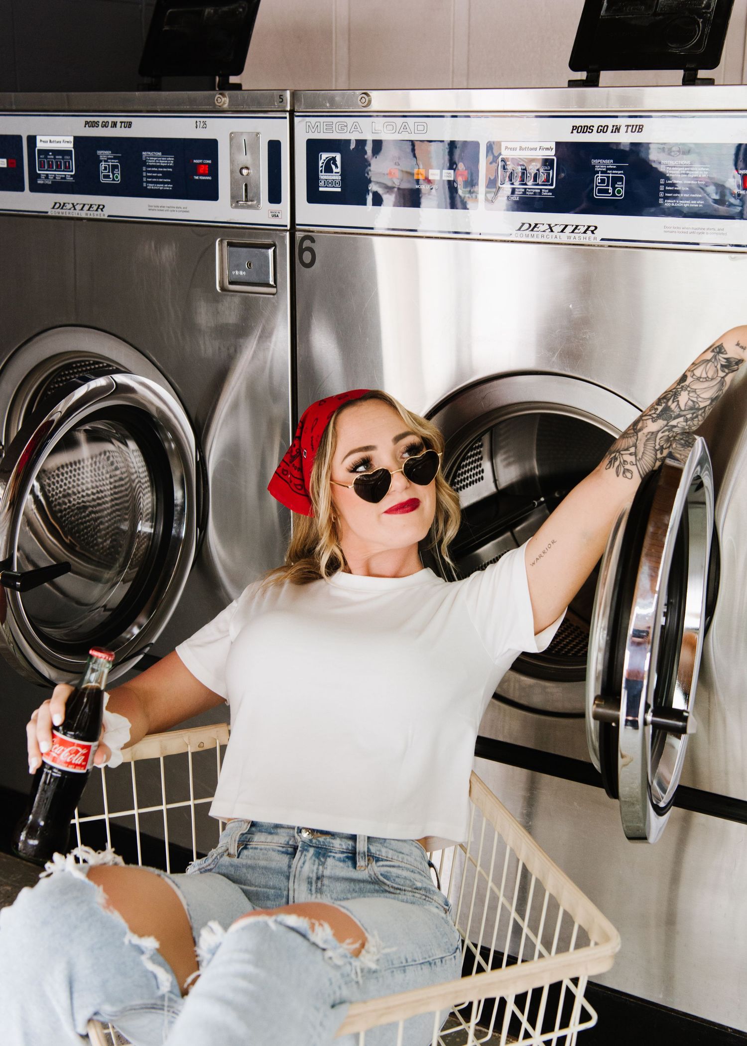 Person relaxing in retro laundromat with sunglasses and red bandana while holding a beverage against washing machines.