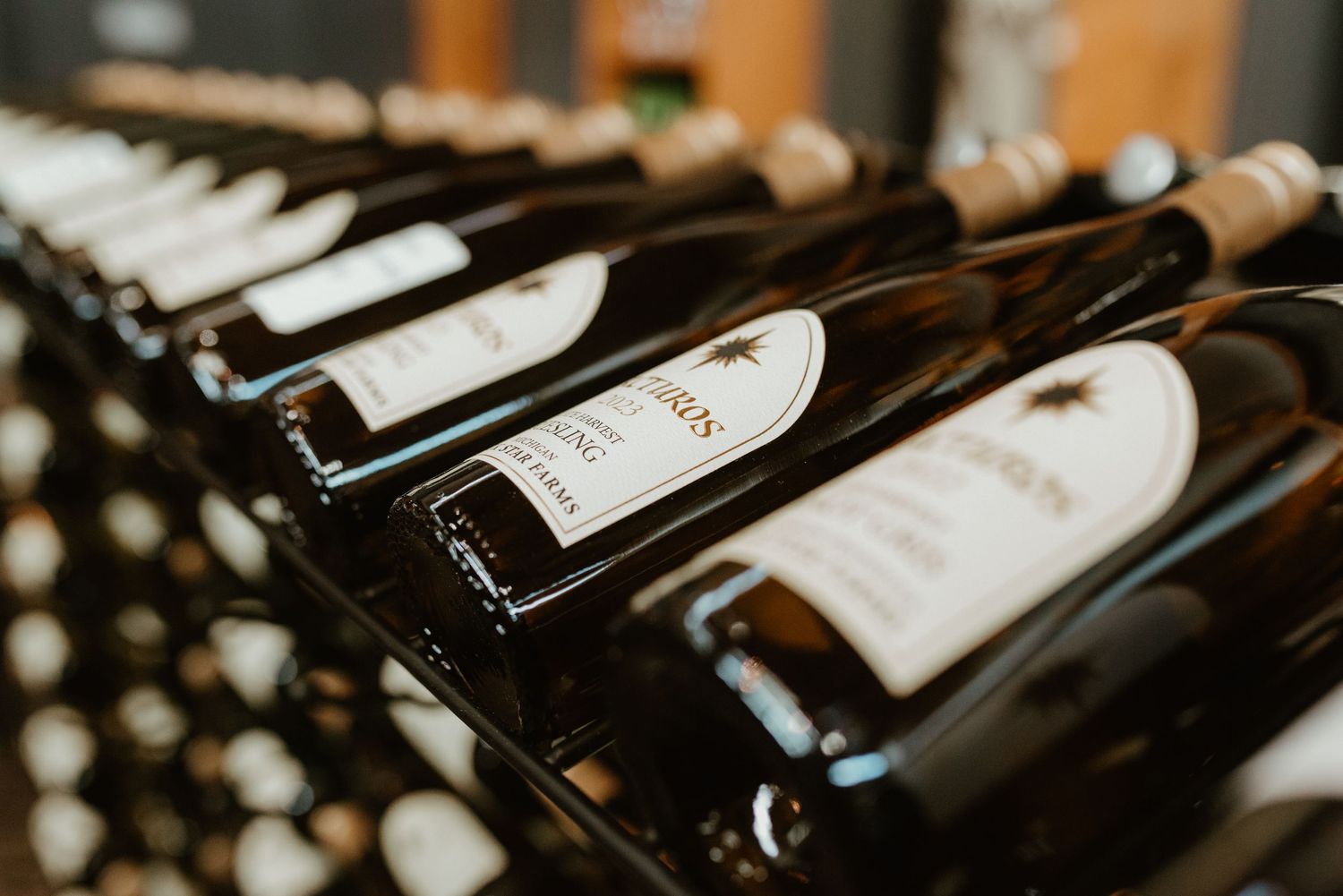 Dark wine bottles with white labels arranged in diagonal rows on a wine rack shelf display.