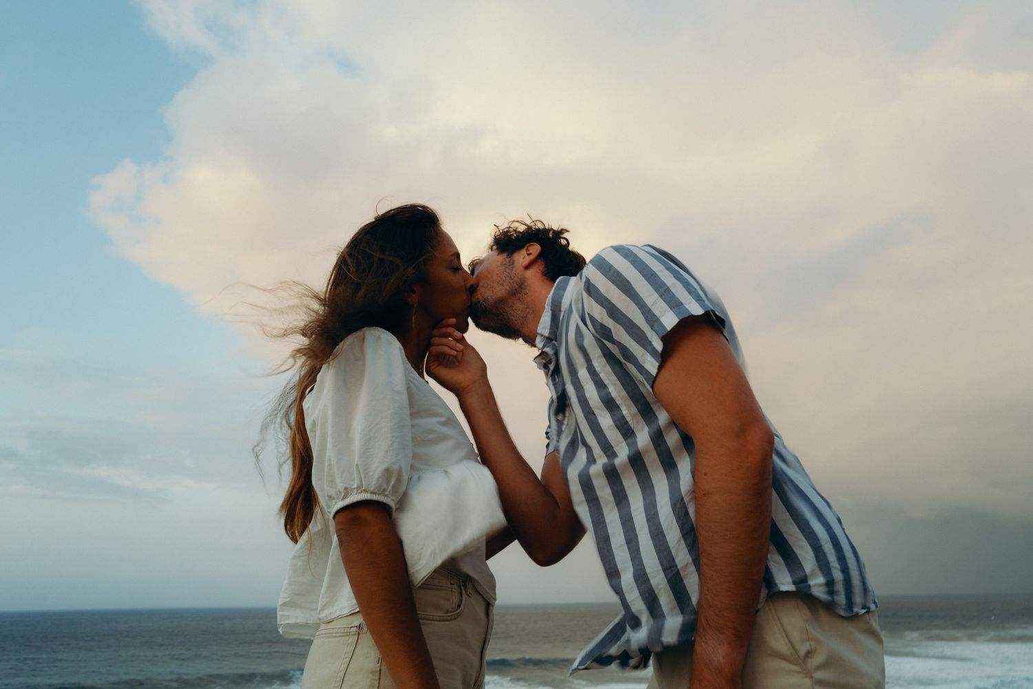 Couple sharing an intimate moment against an ocean sunset backdrop.