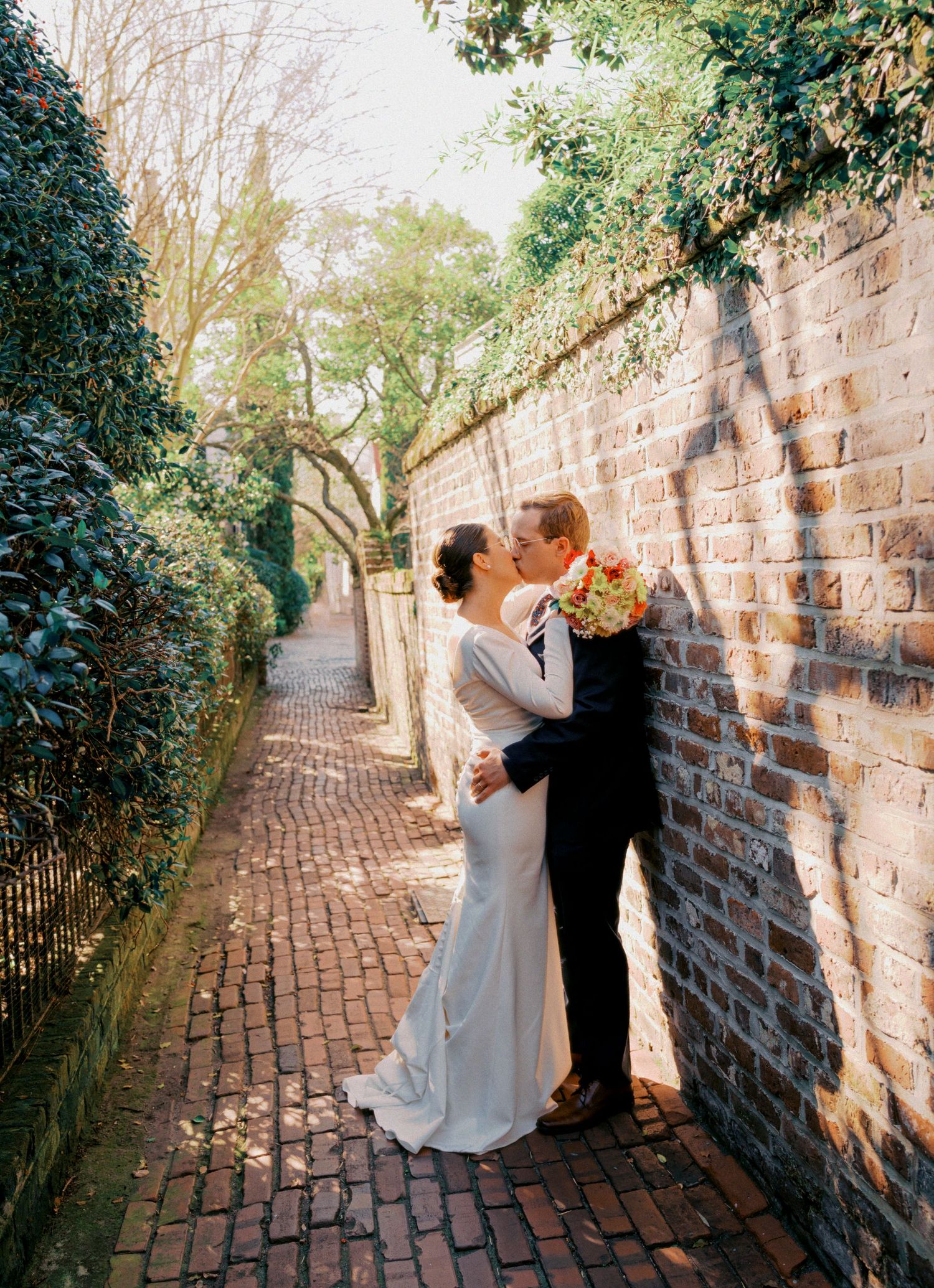 A romantic moment shared on a charming brick pathway lined with green ivy and historic stone walls in golden sunlight.