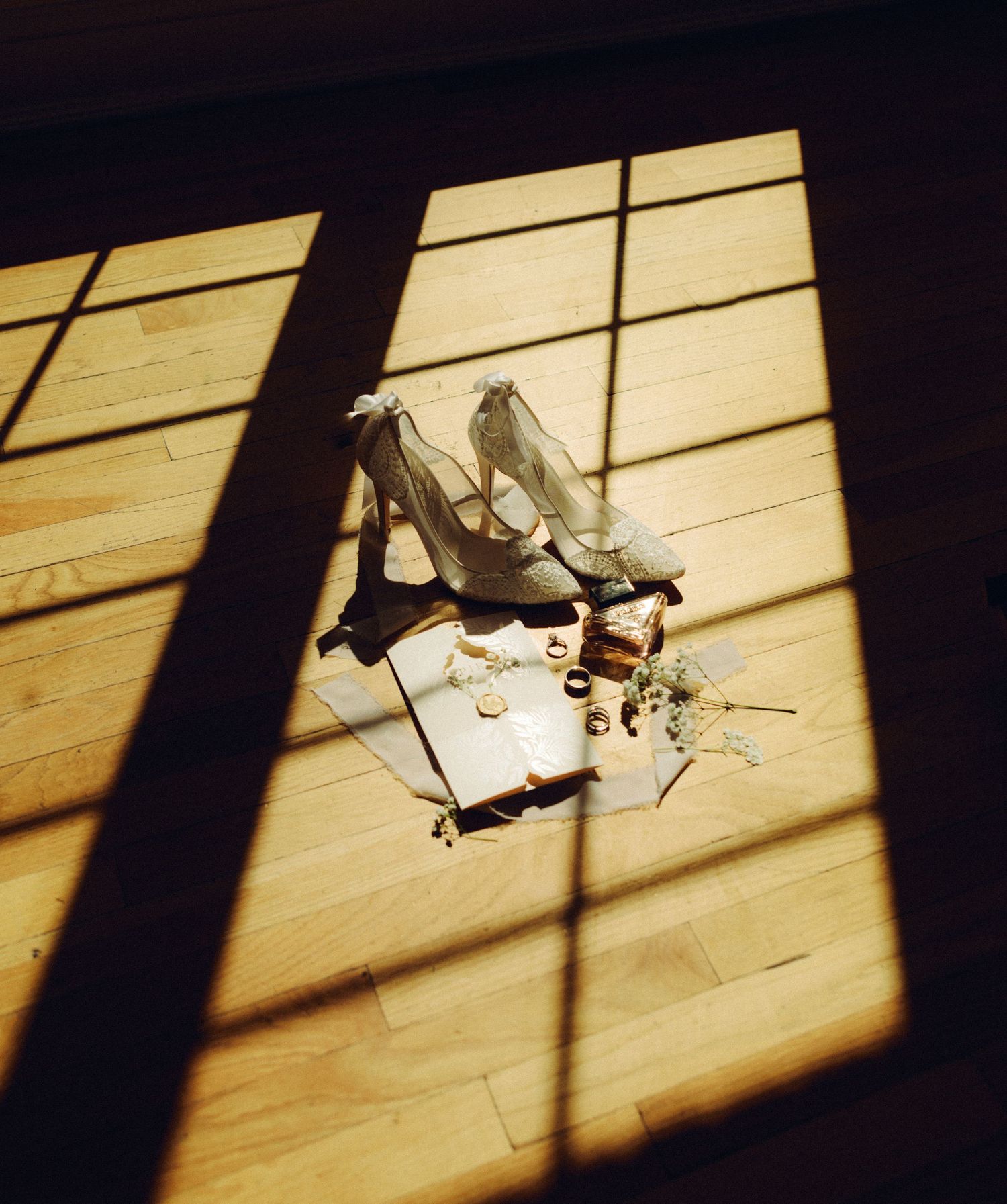 Wedding shoes and accessories casting dramatic shadows on a wooden floor in sunlight.
