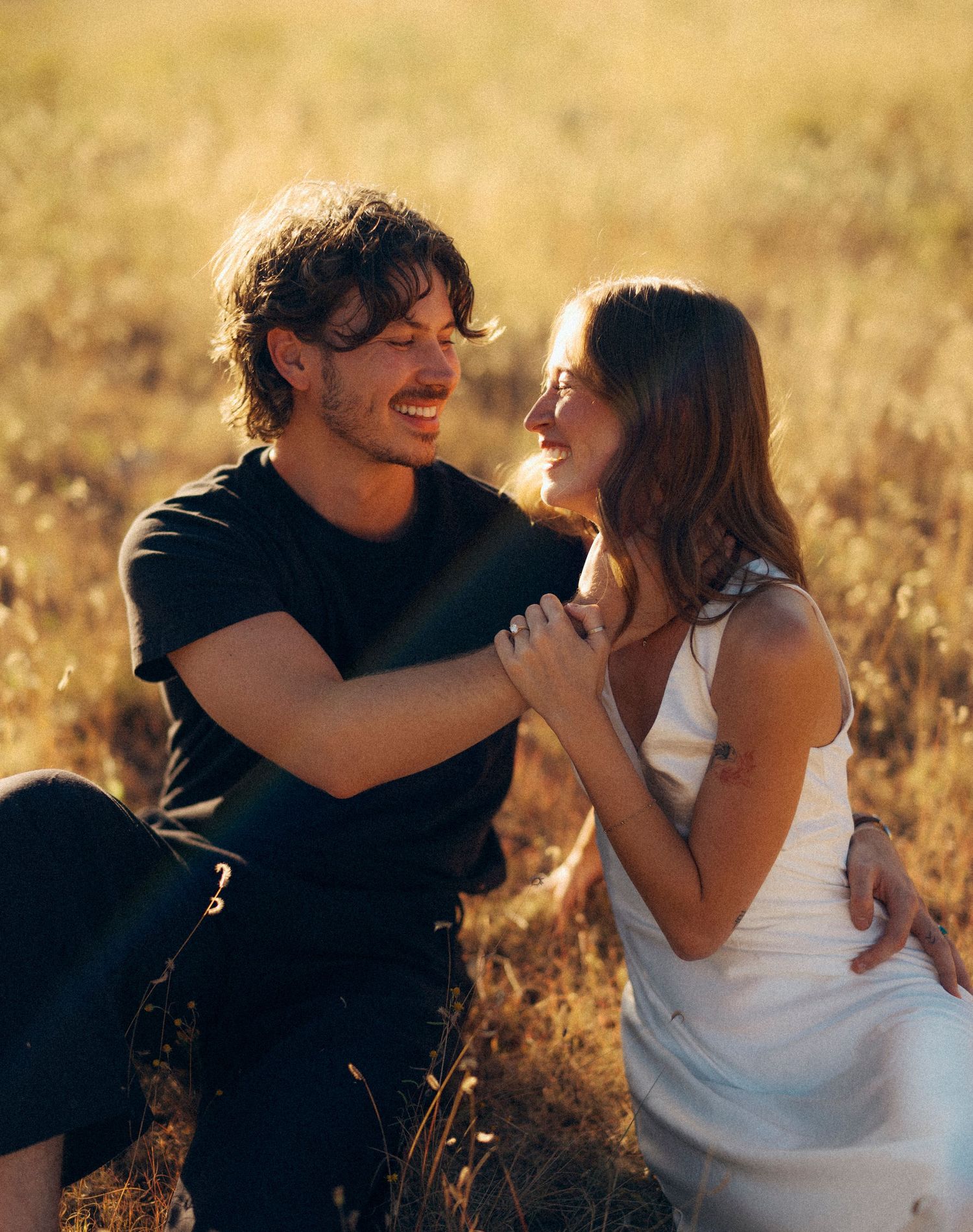 A couple shares a joyful moment together in a sun-drenched field of golden grass.