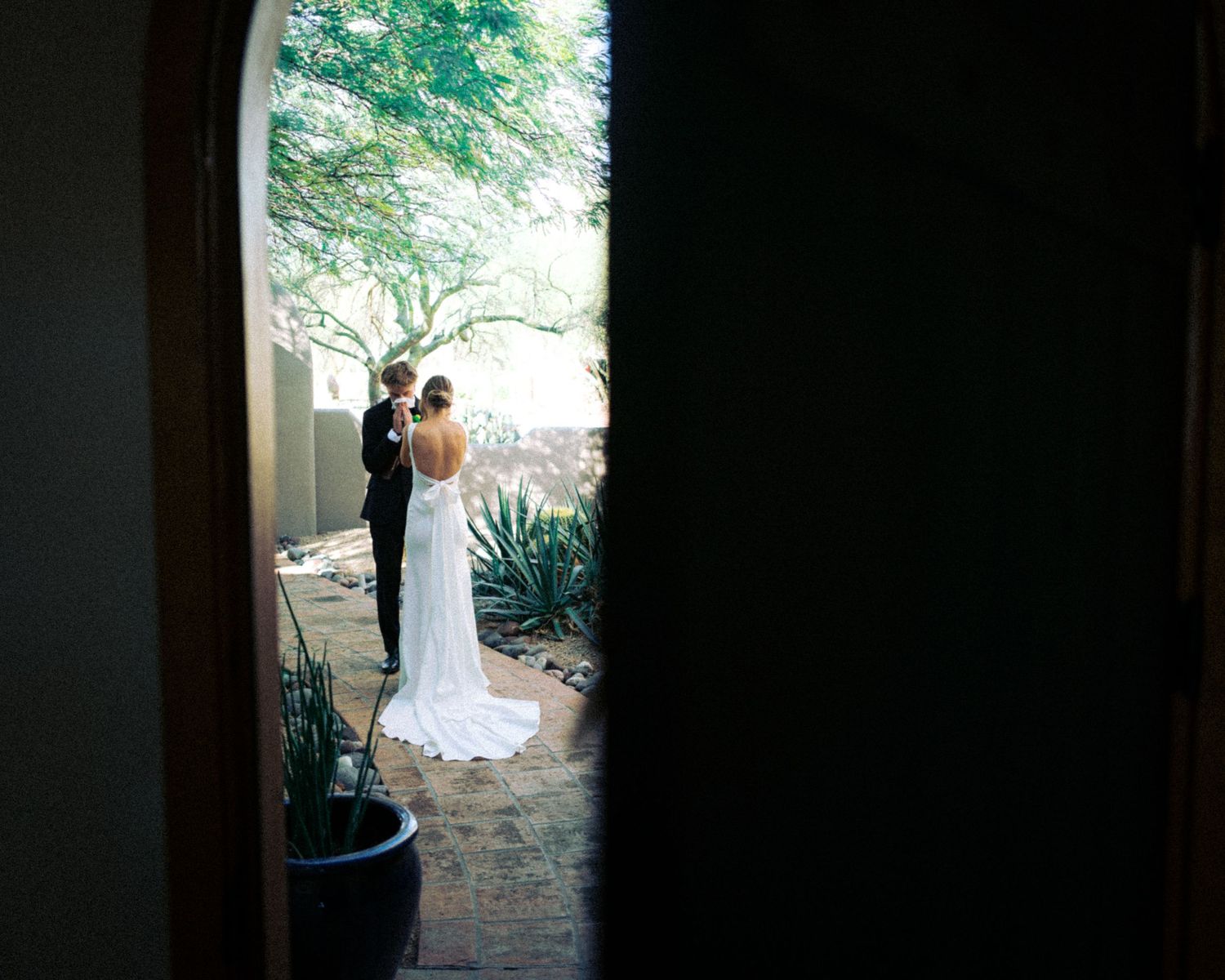 A wedding couple photographed through a doorway against garden landscaping.