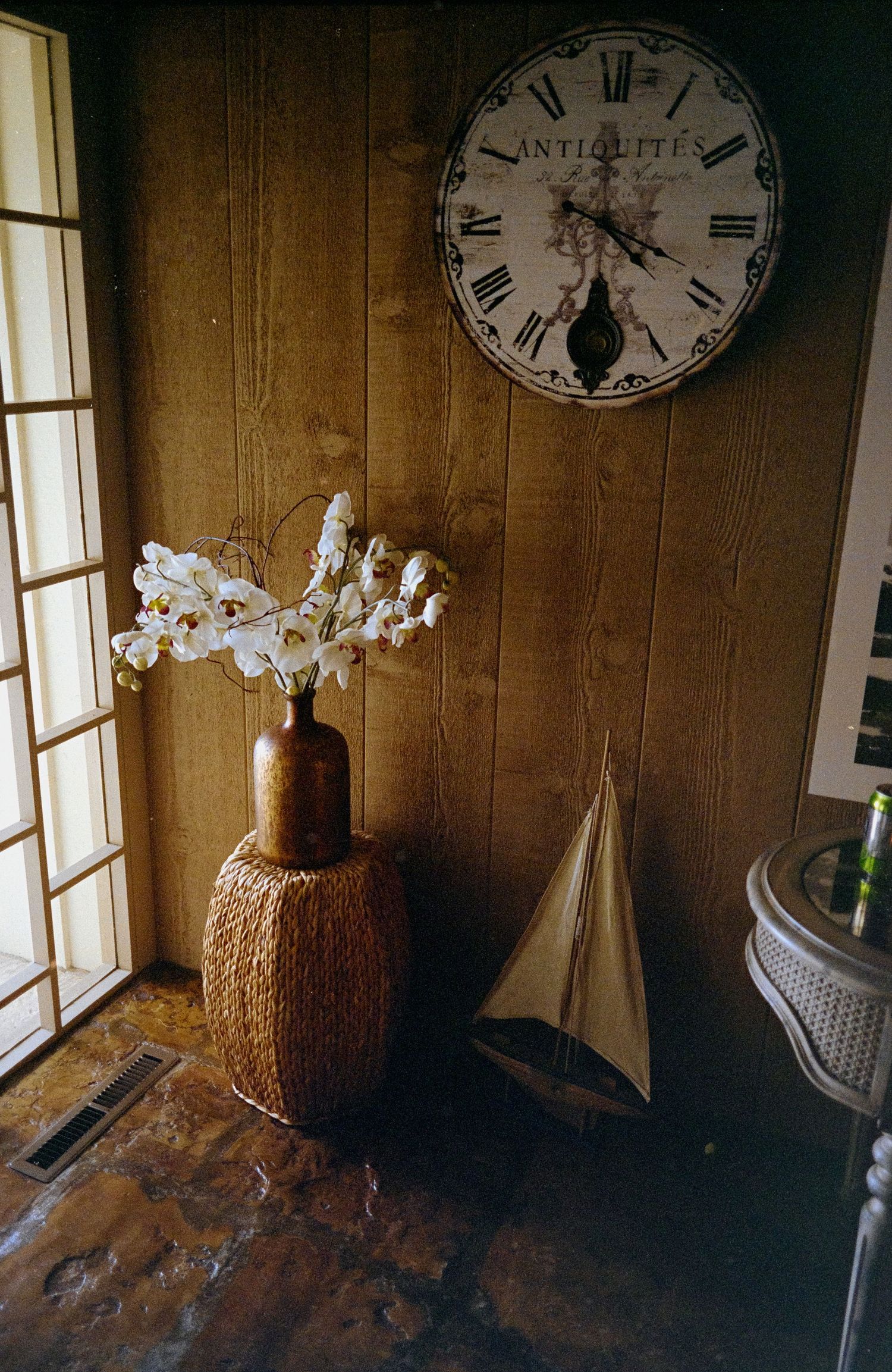 Vintage room decor with white orchids and antique clock on wooden wall.