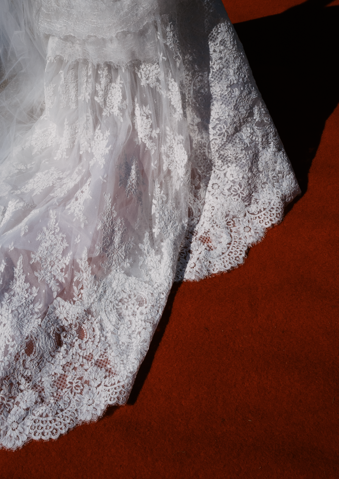 Delicate white lace hem detail of a wedding dress cascading over a rich terracotta colored background.