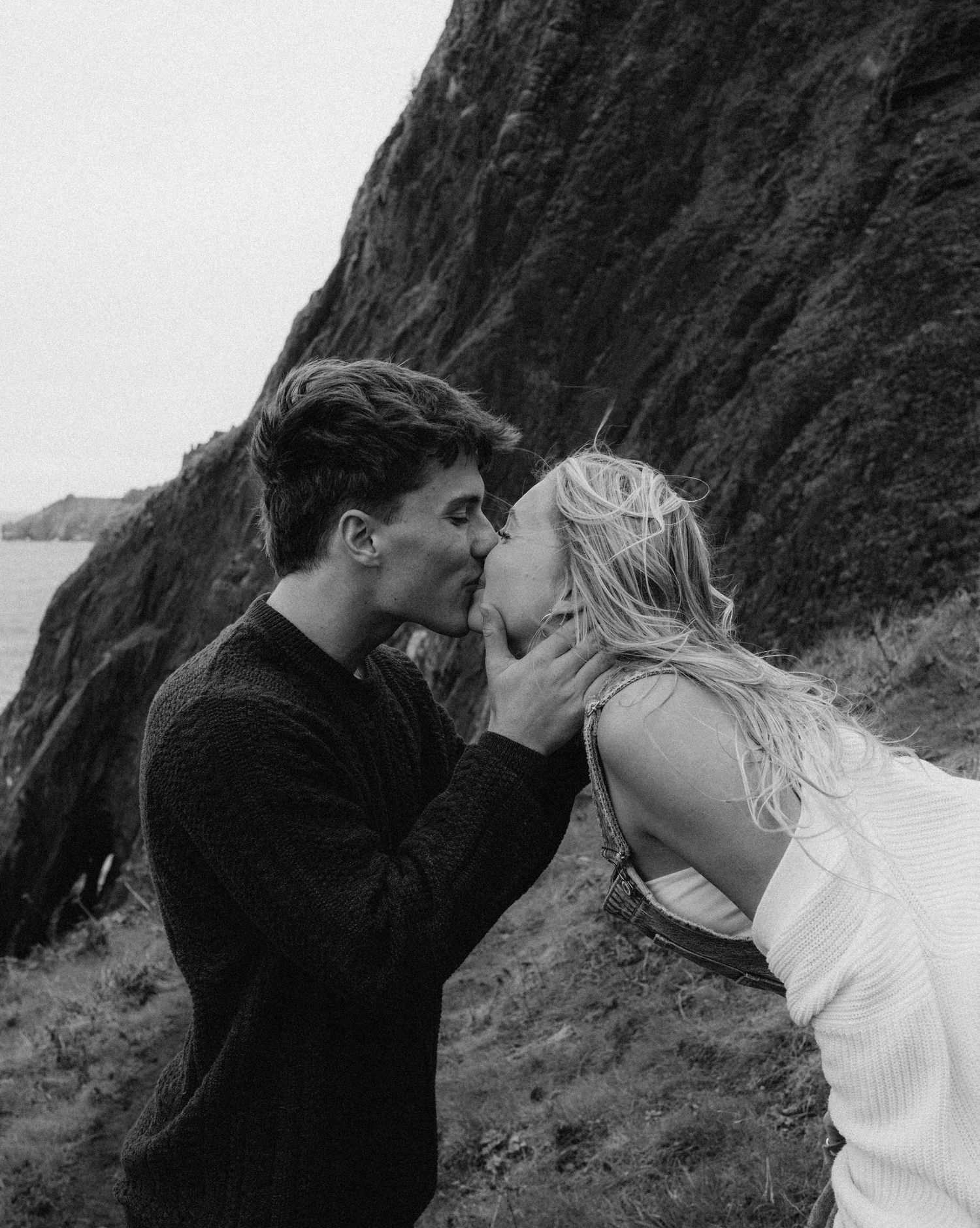 A romantic moment captured in black and white against dramatic coastal cliffs.