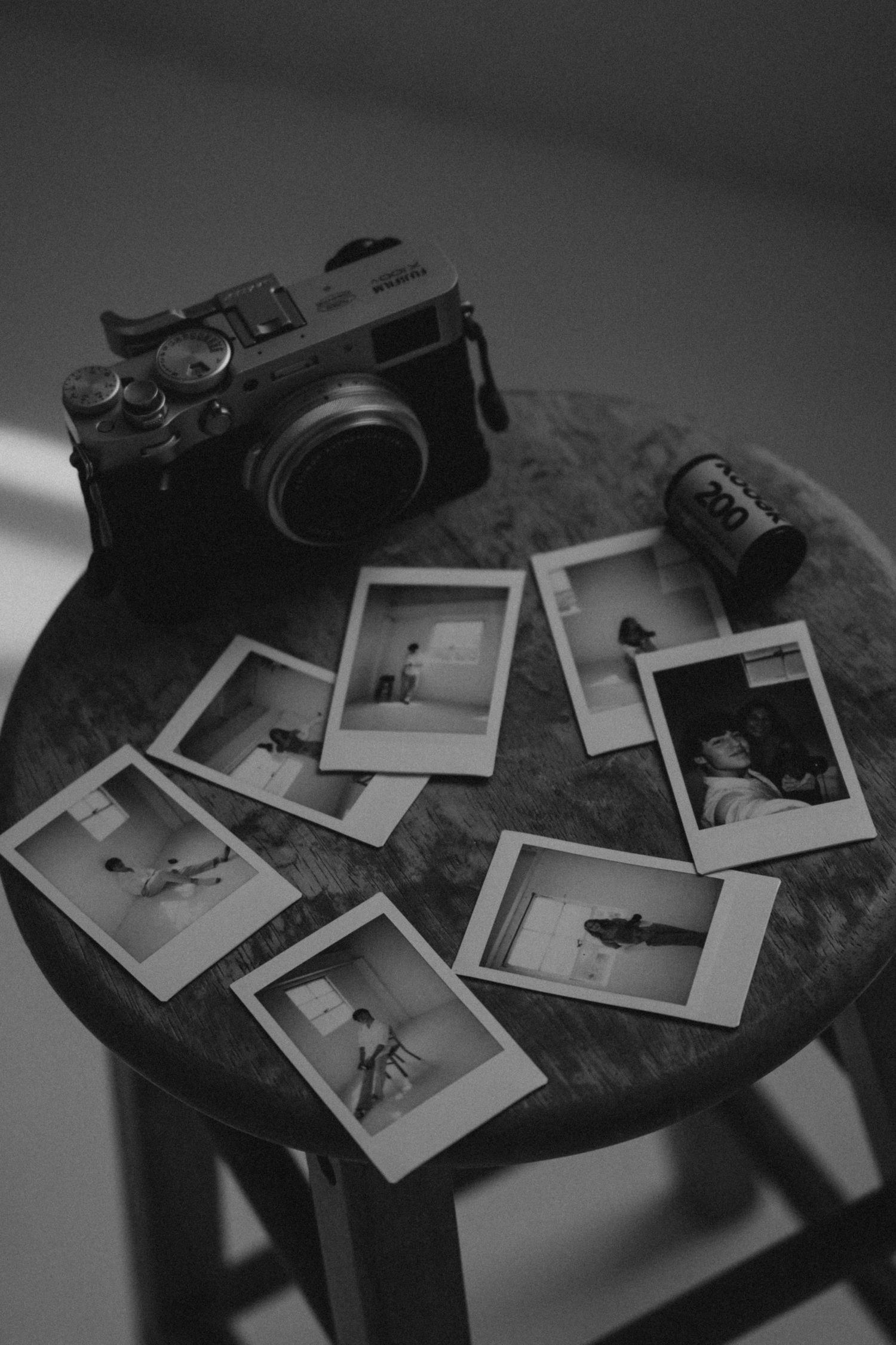 Vintage camera and polaroid photos arranged on a wooden table in black and white.
