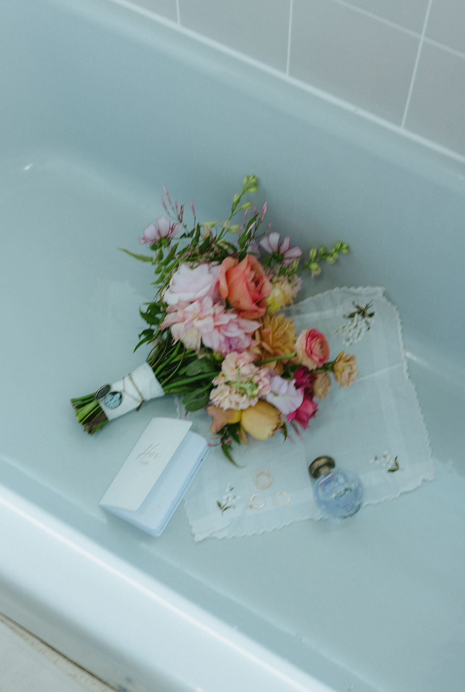 A delicate bouquet of pink and peach flowers with greenery lying in a white bathtub.