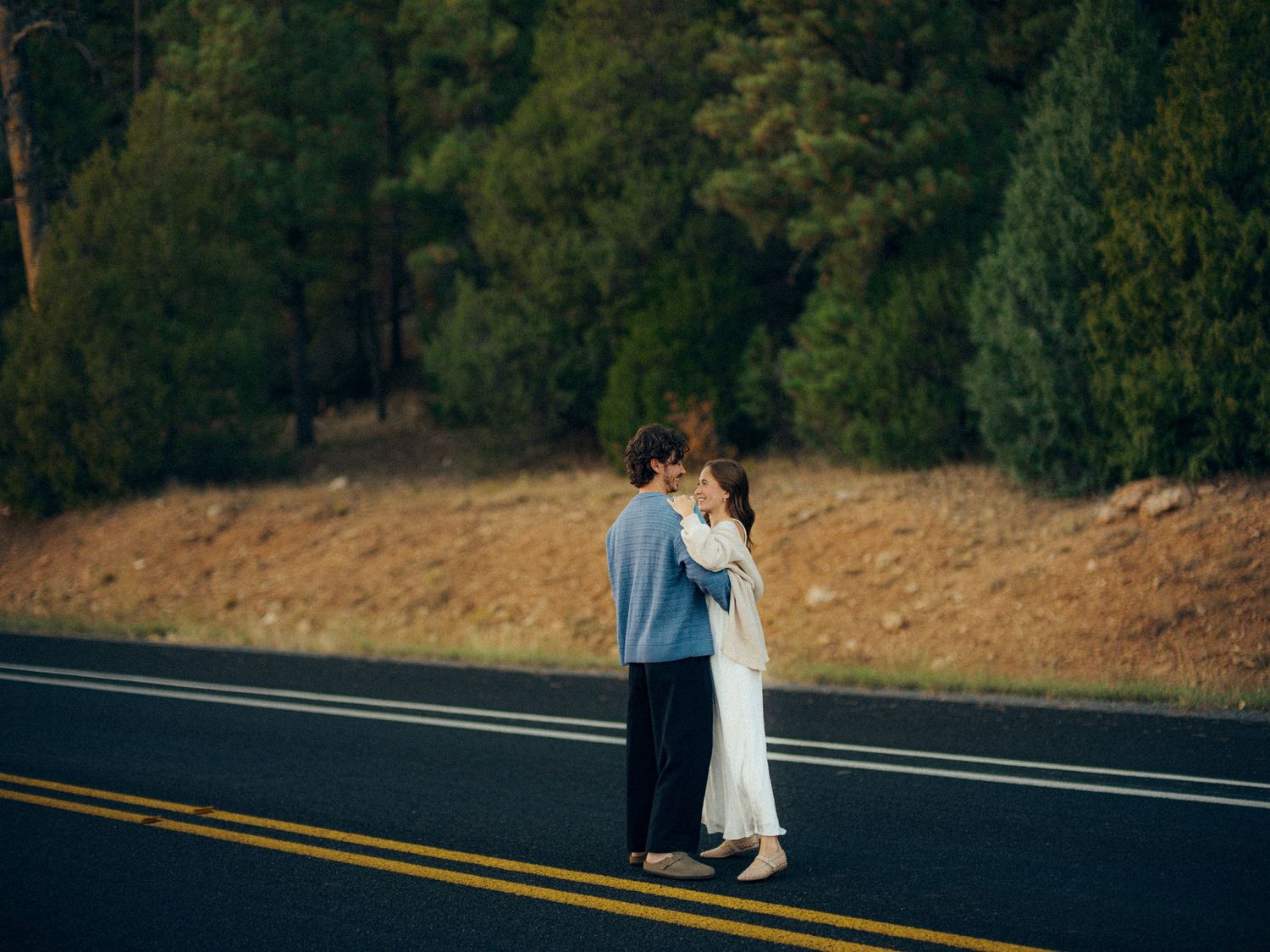 A romantic moment captured on an empty road with trees in the background at dusk.