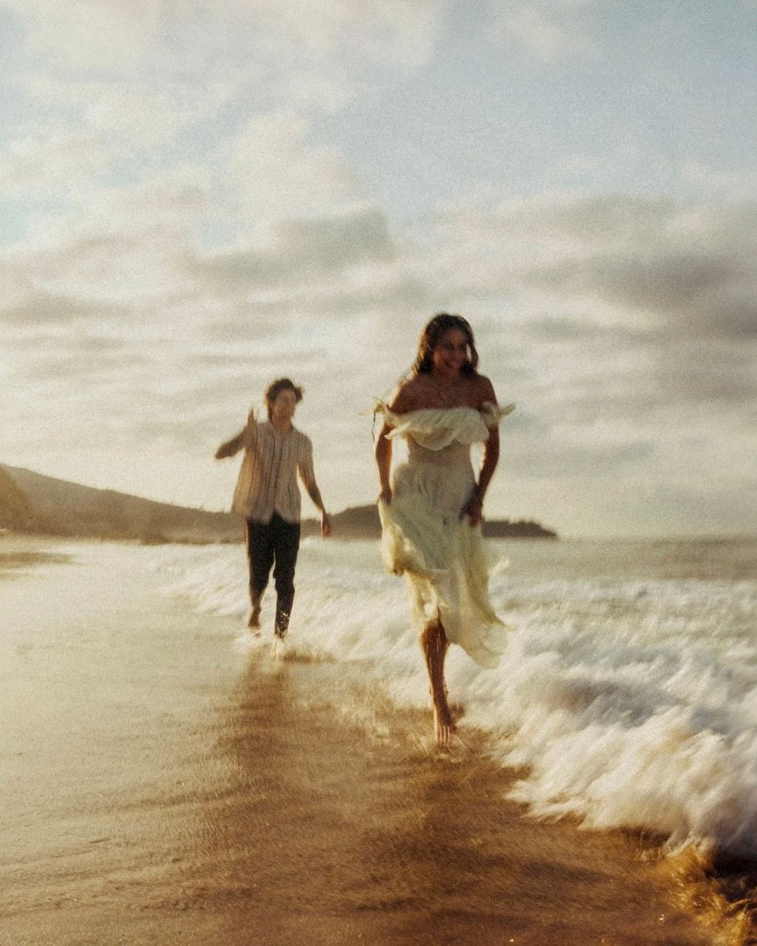 A joyful beach scene with waves crashing as figures run through the surf at sunset.