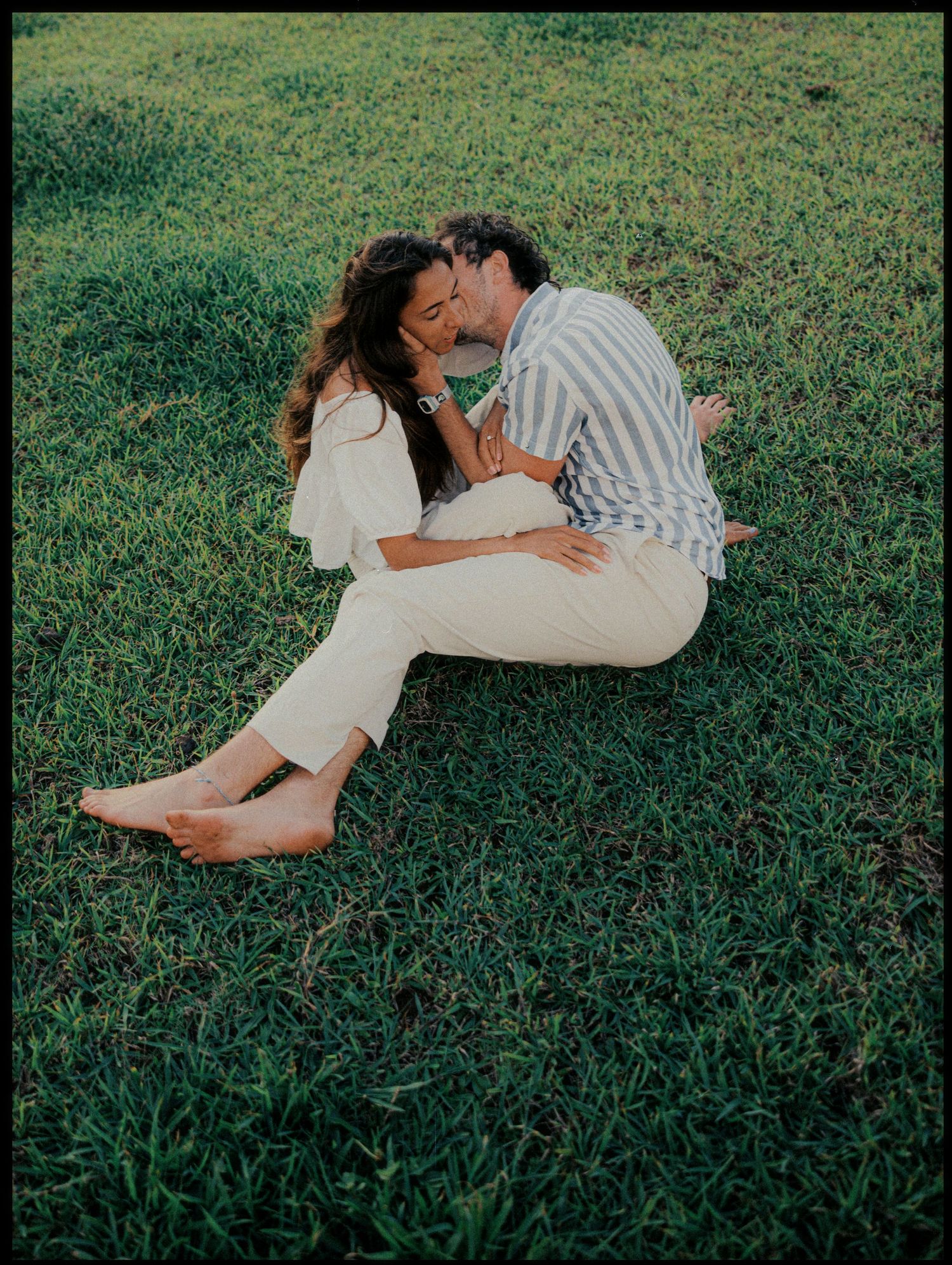 Romantic couple embracing on grass in casual summer outfits.