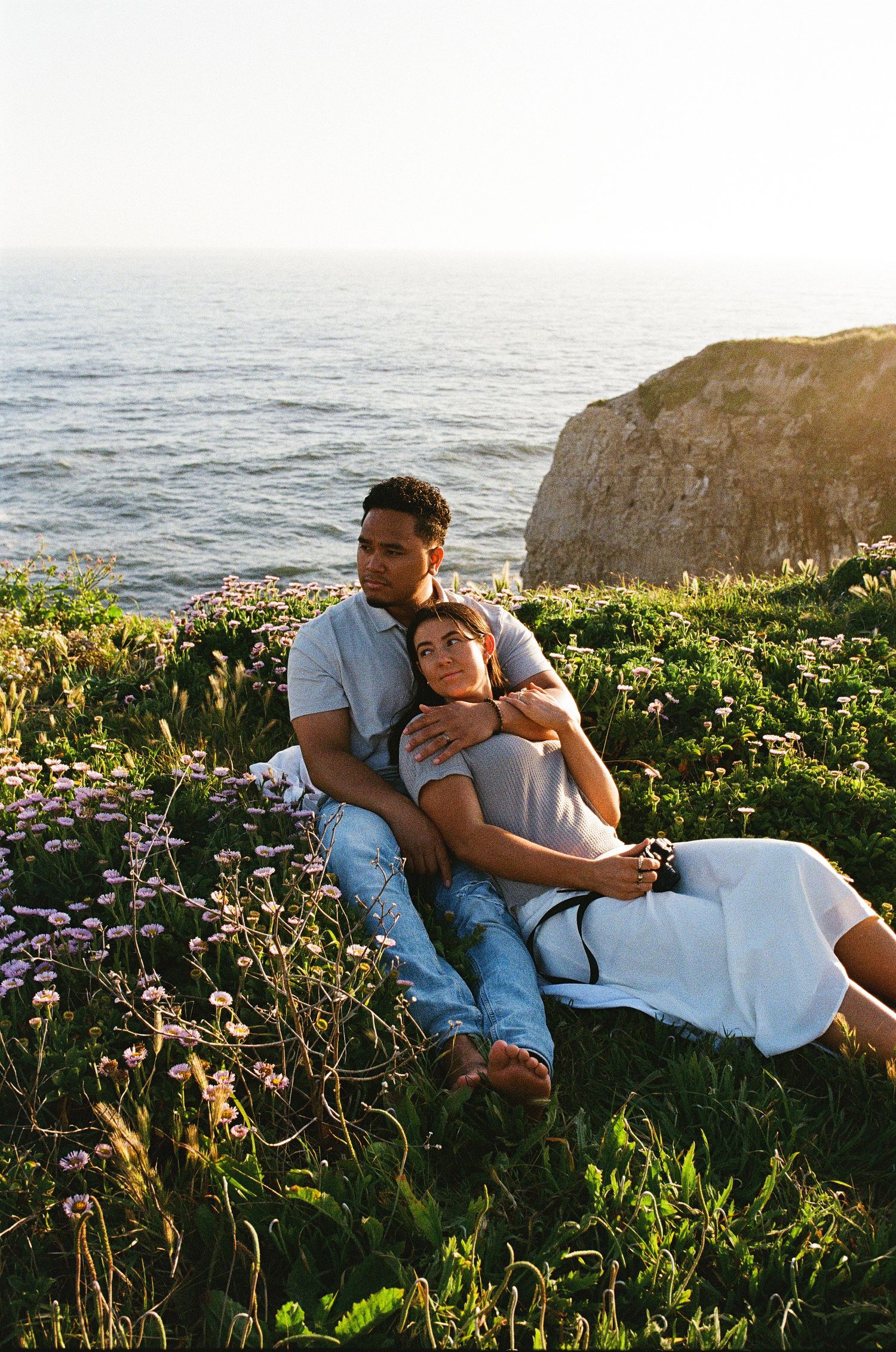 A couple relaxing on a coastal cliff overlooking the ocean at sunset.